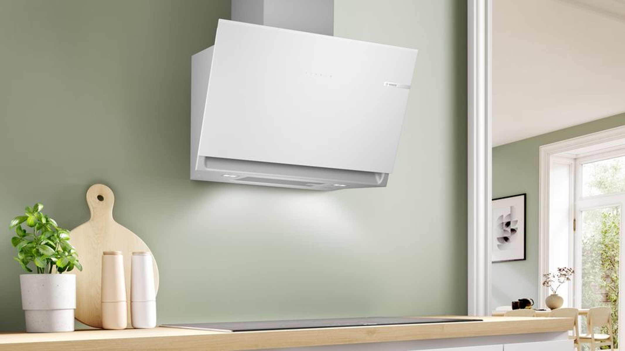 Una campana extractora blanca montada en una pared verde claro sobre una placa de cocina, con encimera de madera.
