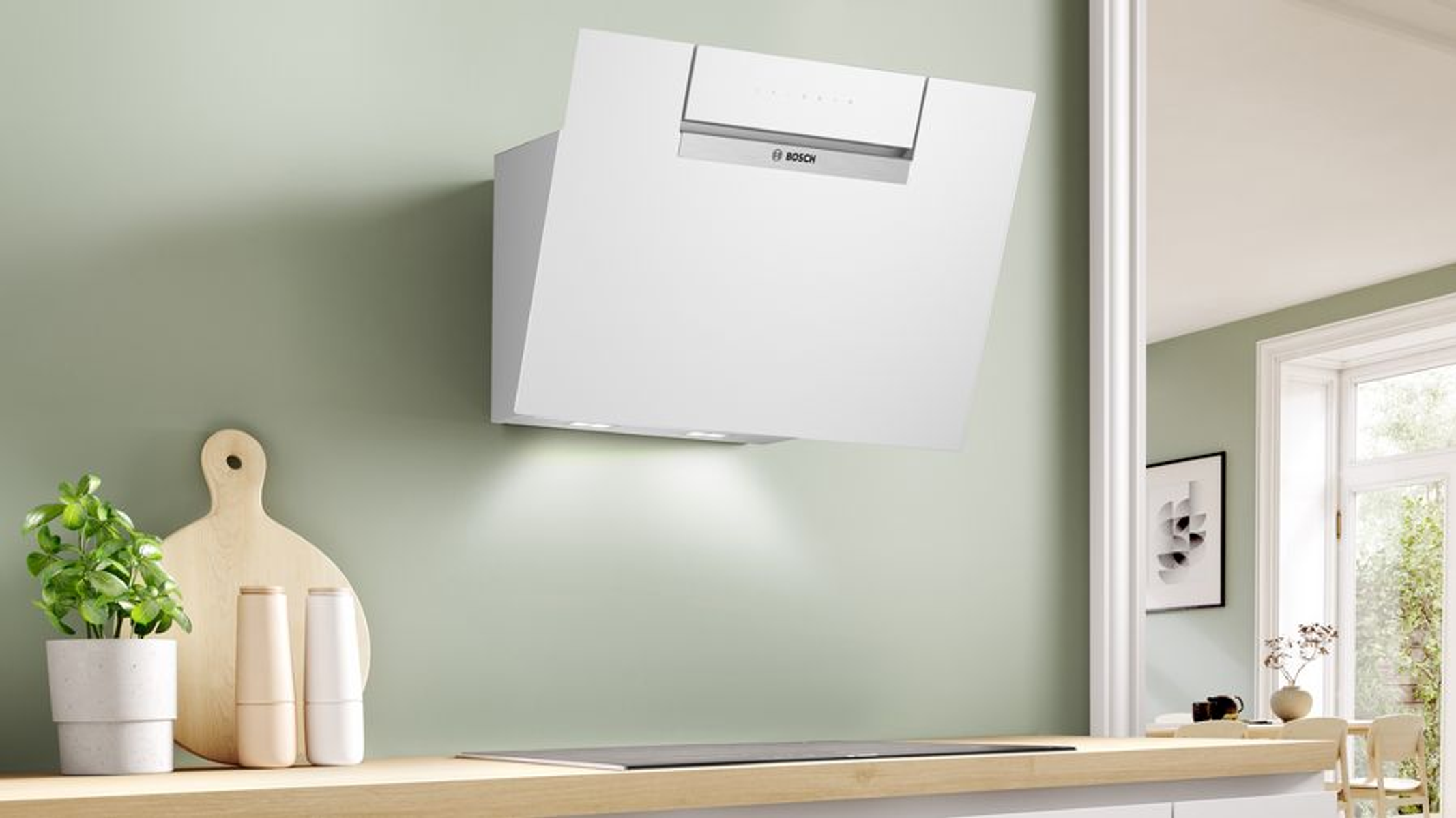 Campana extractora Bosch blanca en pared verde. Estante de madera con plantas y botellas en primer plano.