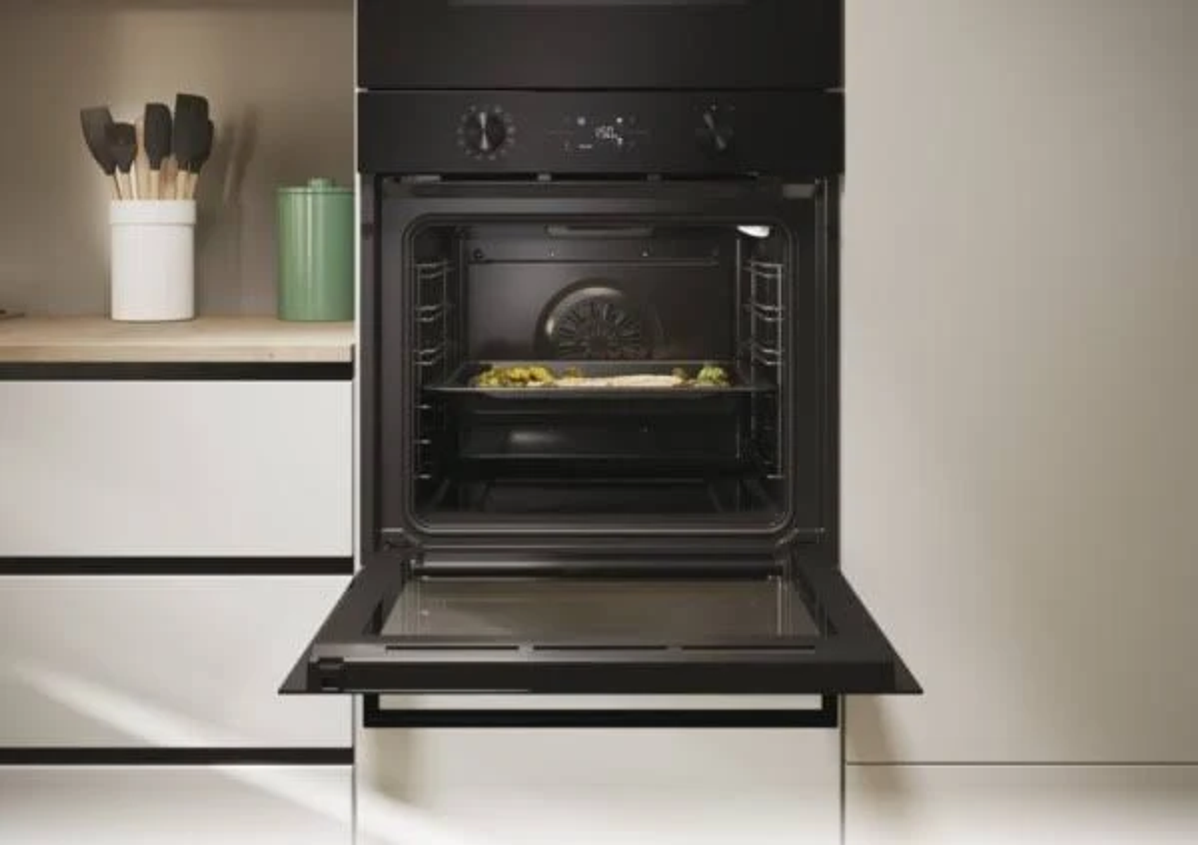 Horno abierto con comida dentro en una bandeja. Interior de cocina con accesorios.
