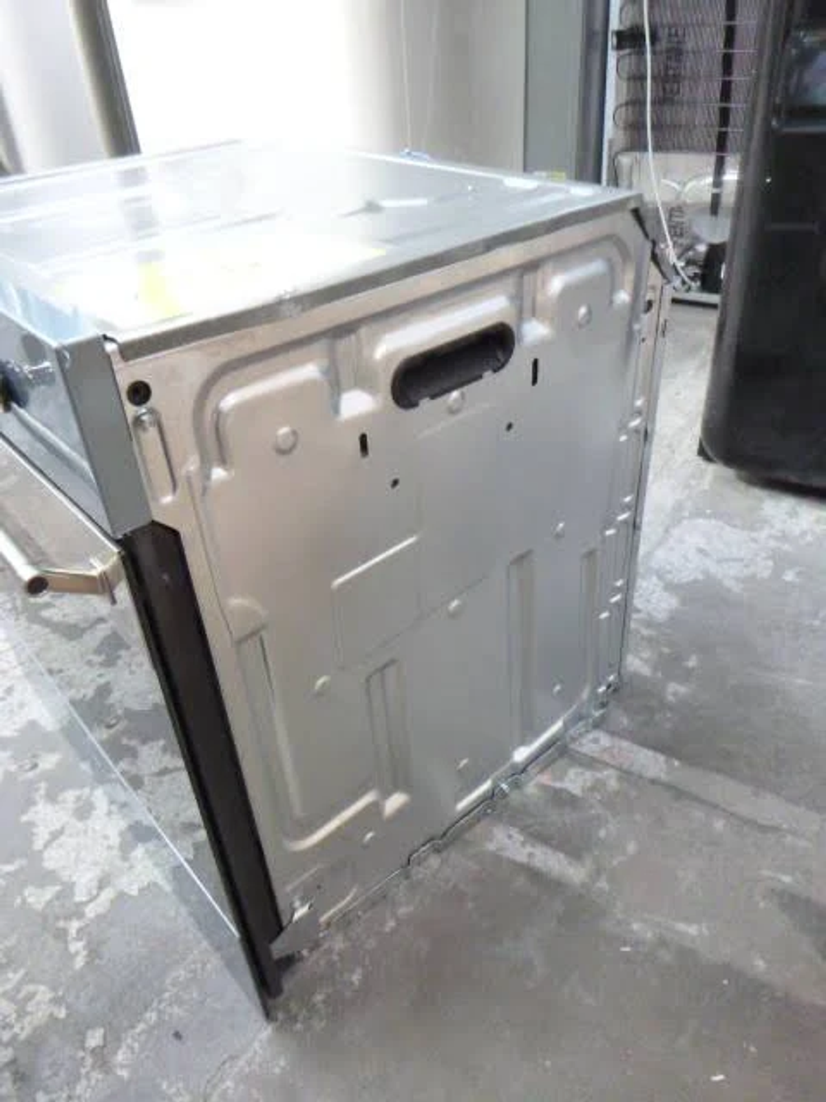 Vista trasera de un horno, mostrando la carcasa metálica y el asa, ligeramente inclinada.