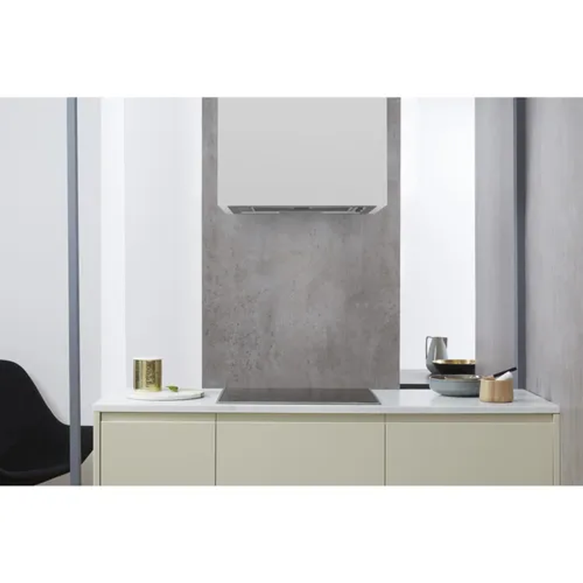 Kuchnia z białym okapem nad czarną płytą grzewczą i betonową ścianą. Beżowe szafki.