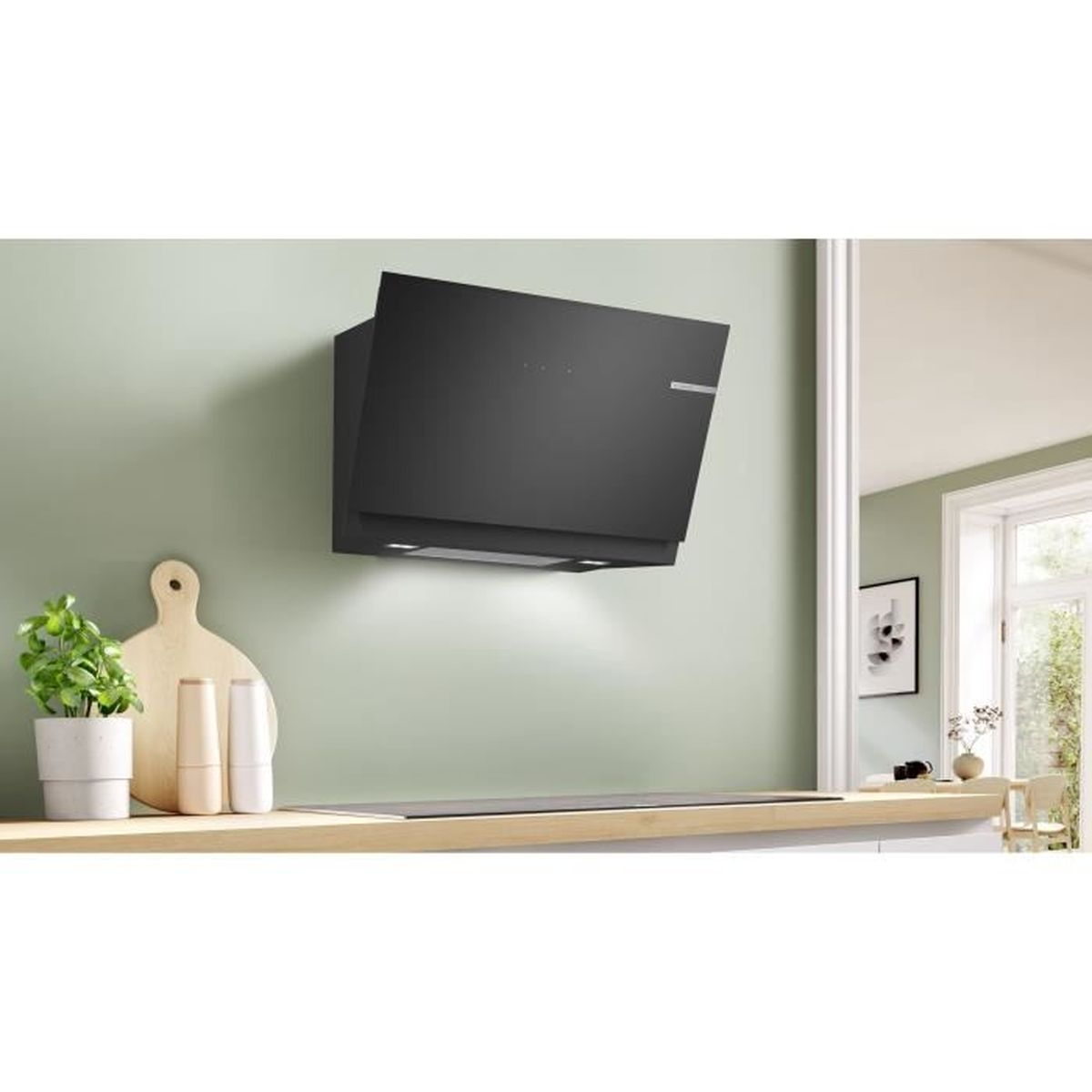 Black range hood mounted on a green wall above a countertop, with a plant and decor.