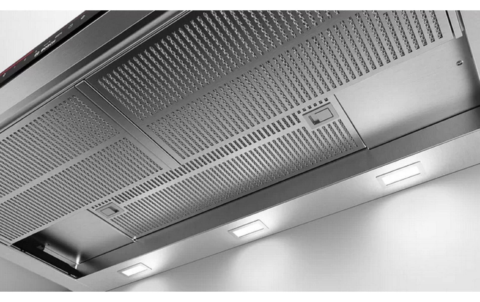 Primer plano de una campana extractora de acero inoxidable con rejilla y luces. El fondo es una pared blanca.