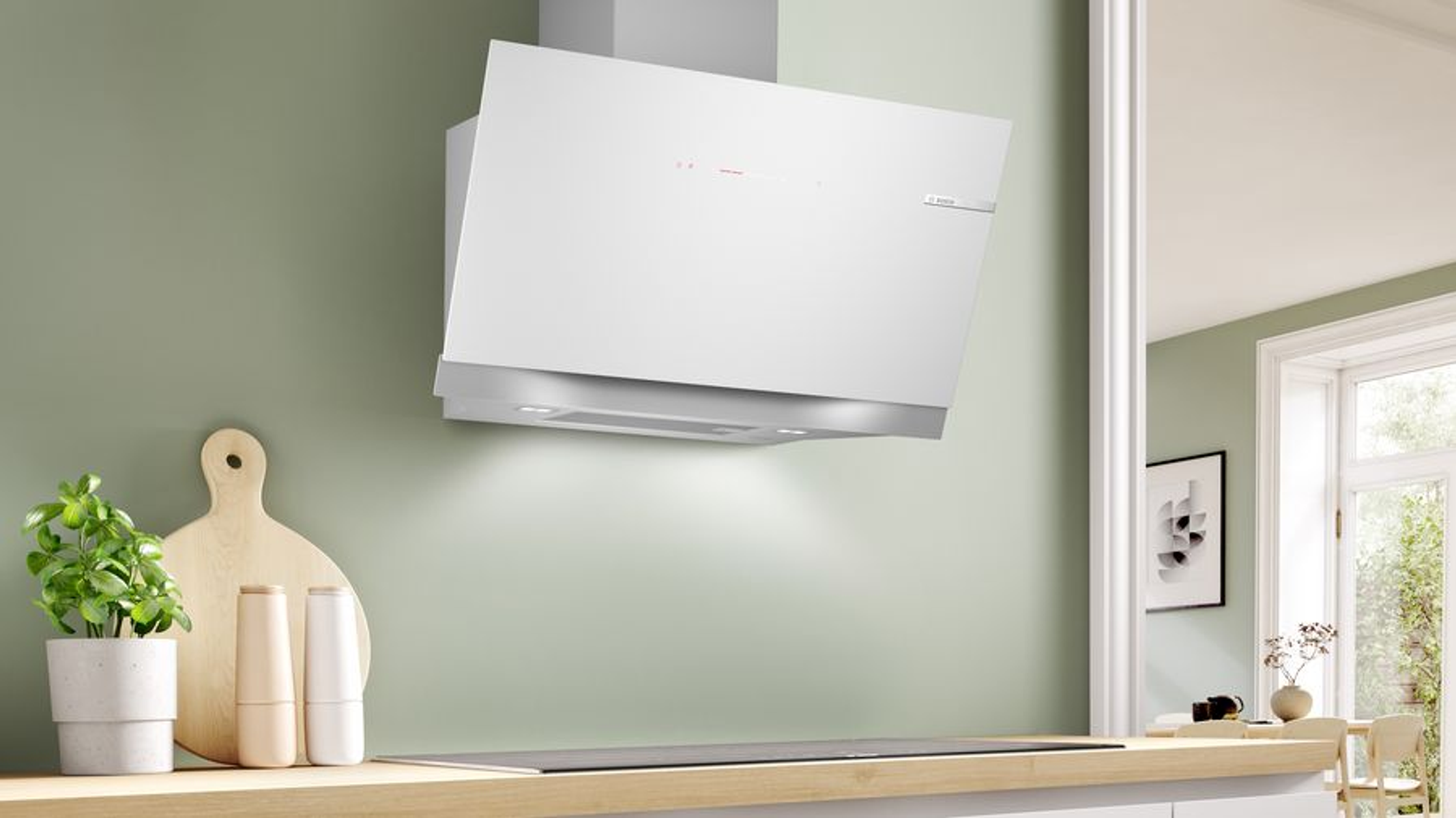 Una campana blanca montada en una pared verde, con una encimera de madera y plantas.