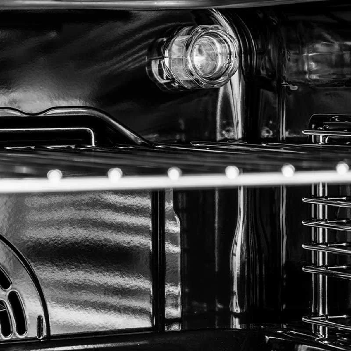 Primer plano del interior del horno. Luz y rejillas metálicas visibles. Fondo negro.