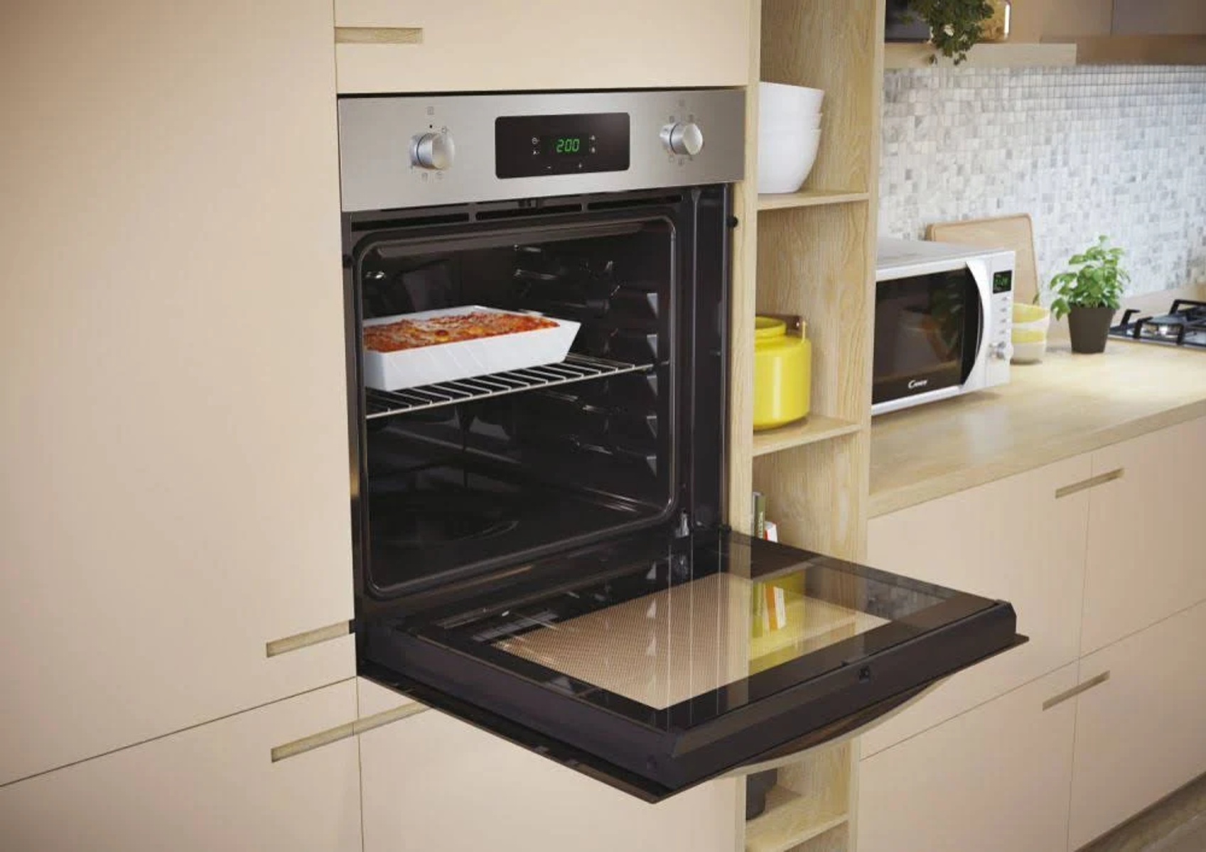 Un forno con un vassoio di cibo, porta aperta, in un ambiente cucina con altri elettrodomestici.