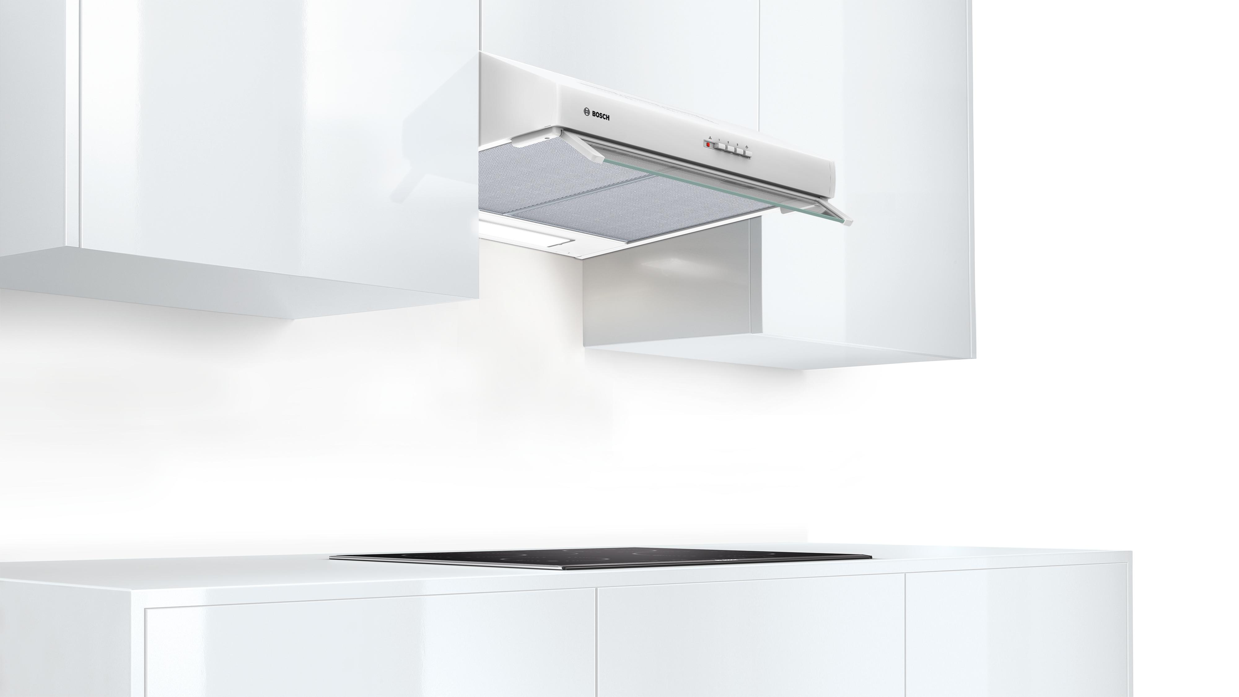 Una scena di cucina con una cappa Bosch installata sopra un piano cottura nero, con mobili bianchi.