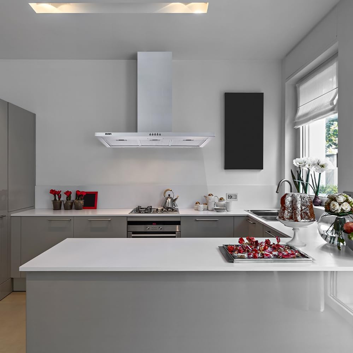 Cocina moderna con campana de acero inoxidable, encimeras blancas y armarios grises.