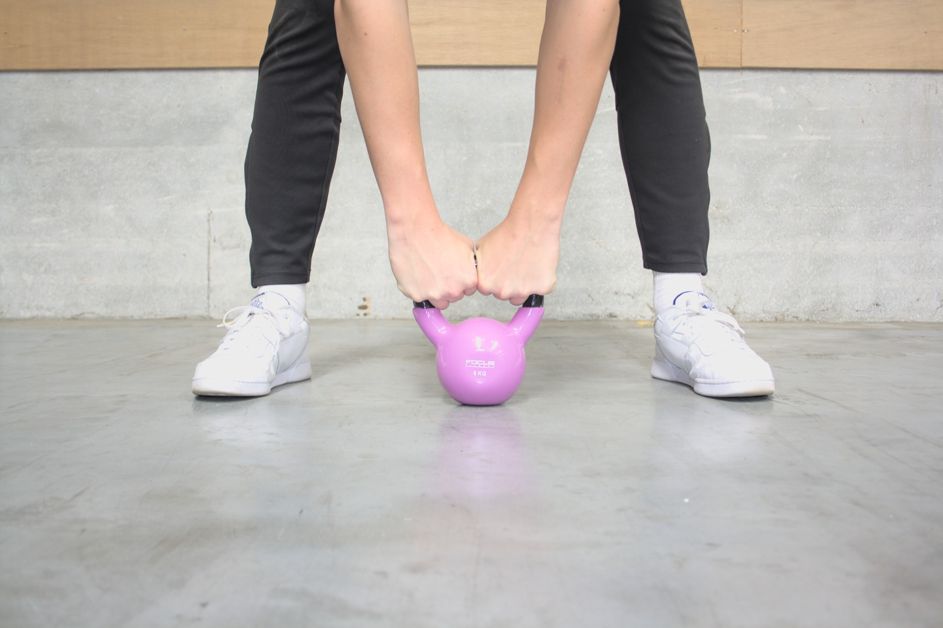 A person is holding a pink kettlebell with both hands while standing.