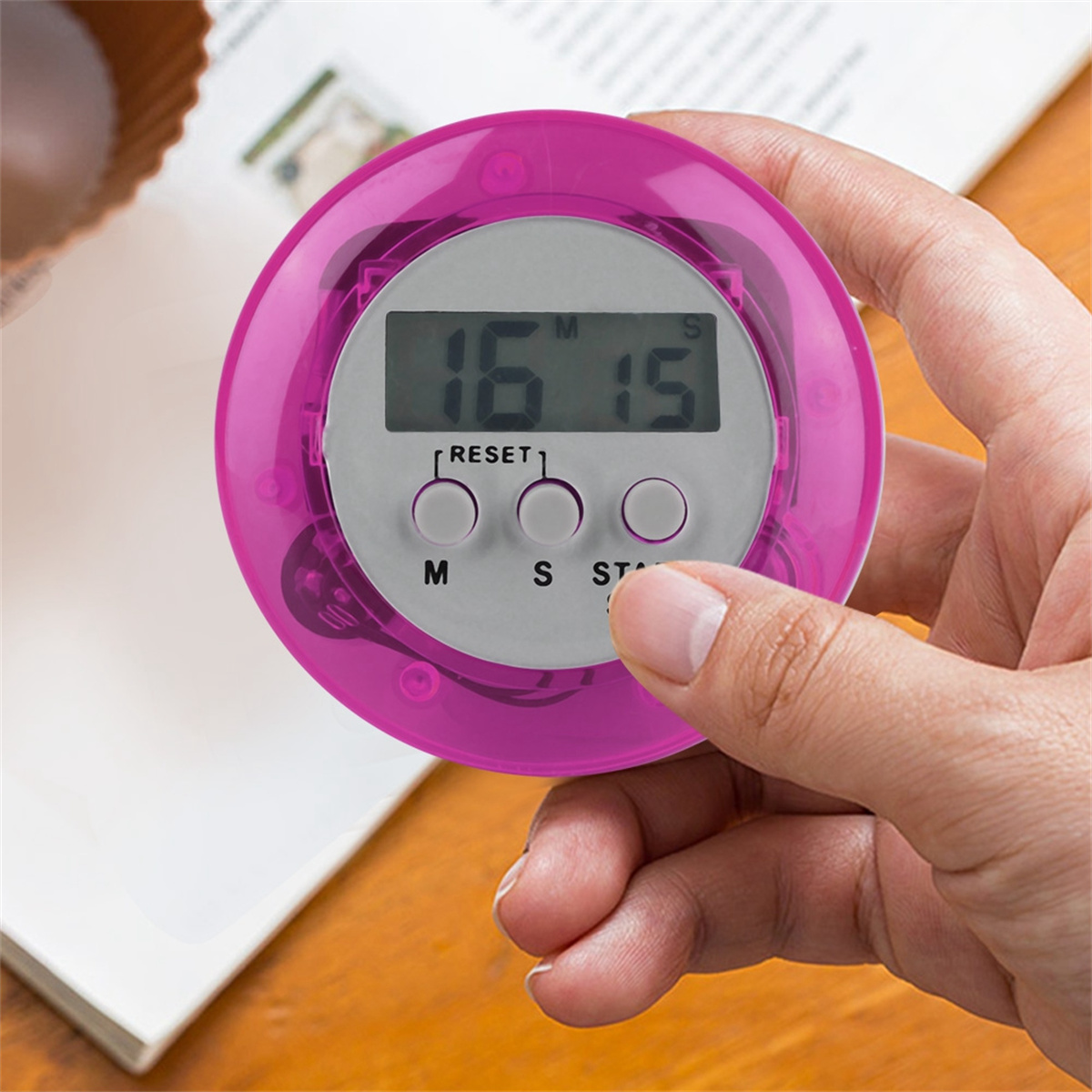 Ein rosa Timer mit Digitalanzeige, die 16:15 anzeigt. Eine Hand hält den Timer mit Tasten für Reset, Minuten und Start.