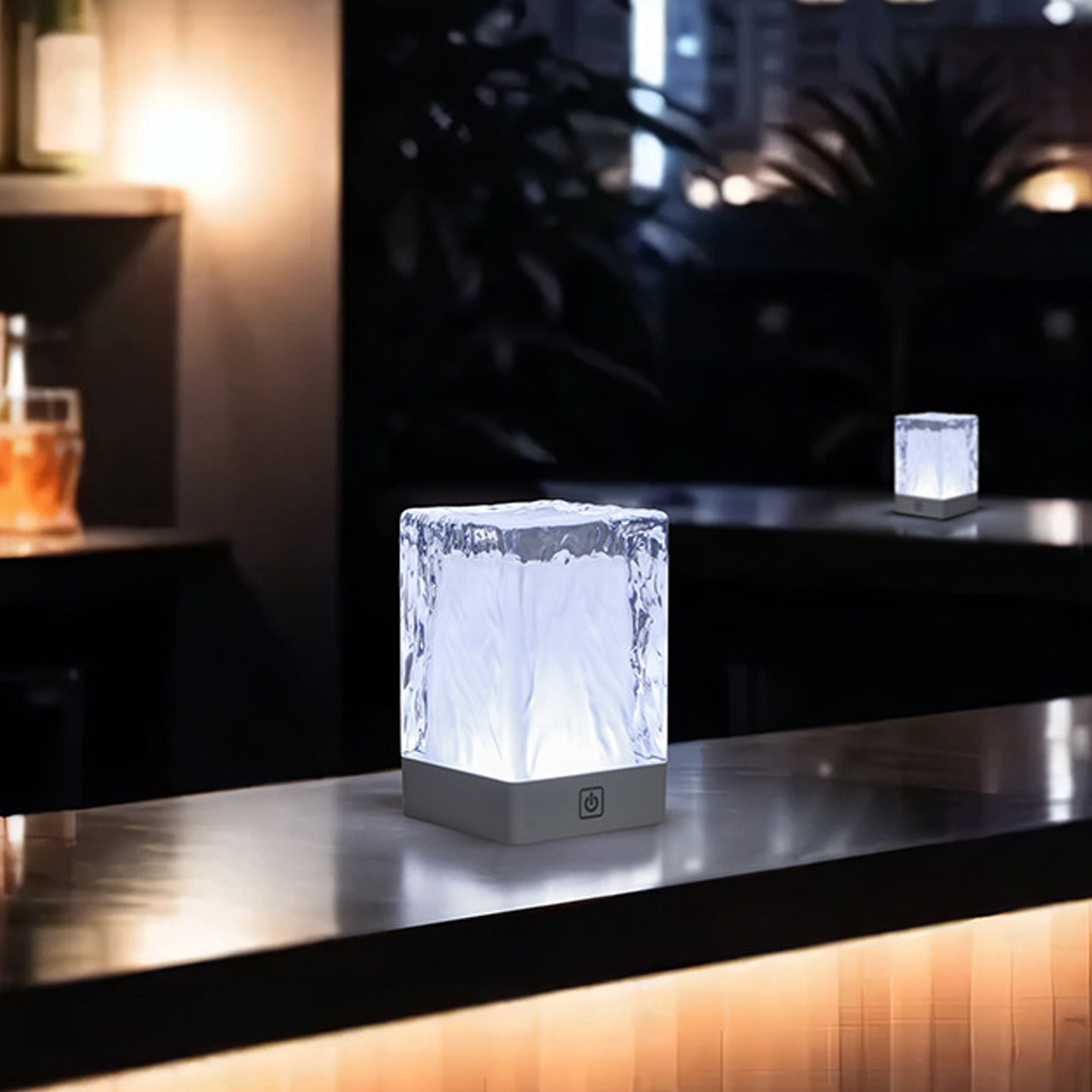 Zwei Lampen in Eiswürfelform auf einer Bar. Die Lampen leuchten mit einem sanften weißen Licht. Dunkler Hintergrund.