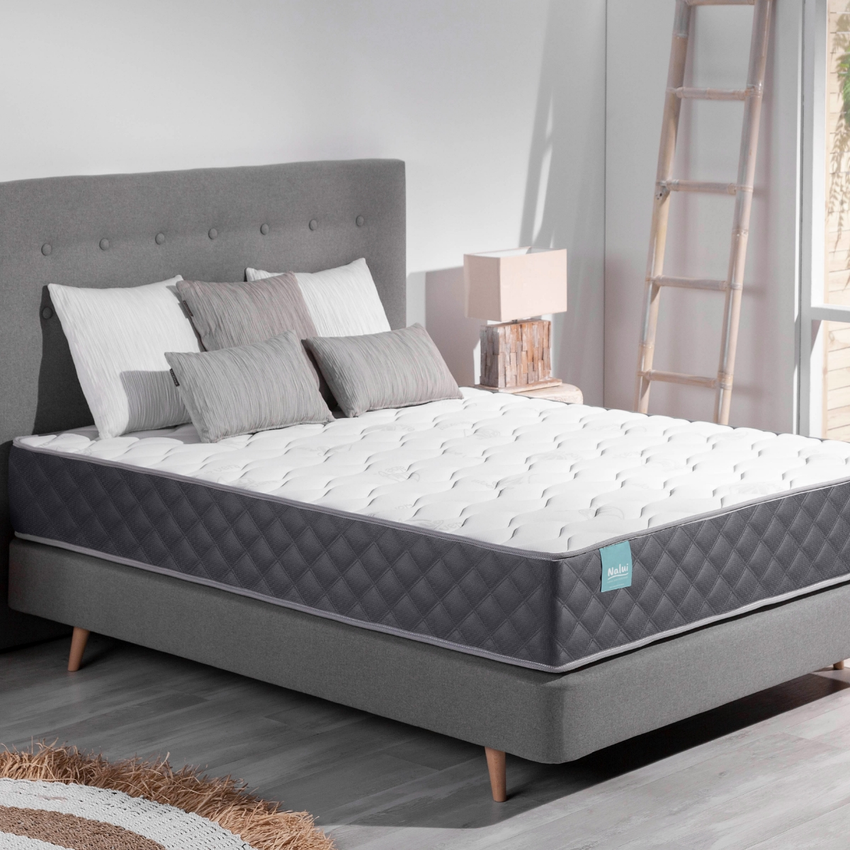 Una cama con cabecero gris, almohadas y un colchón con borde gris.