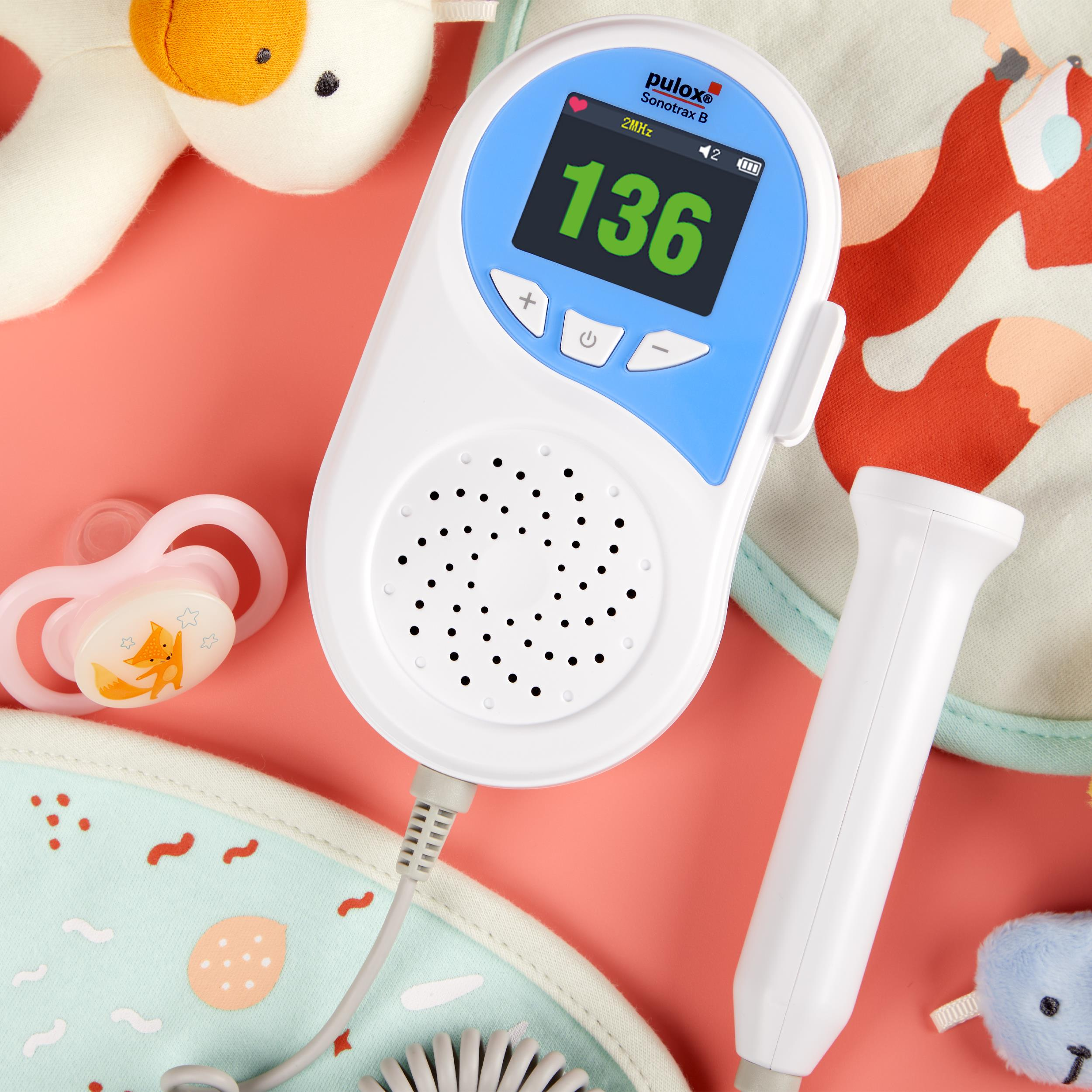 Baby-Herzfrequenzmonitor mit Anzeige von 136 bpm. Der Monitor und das Zubehör liegen auf Rosa.