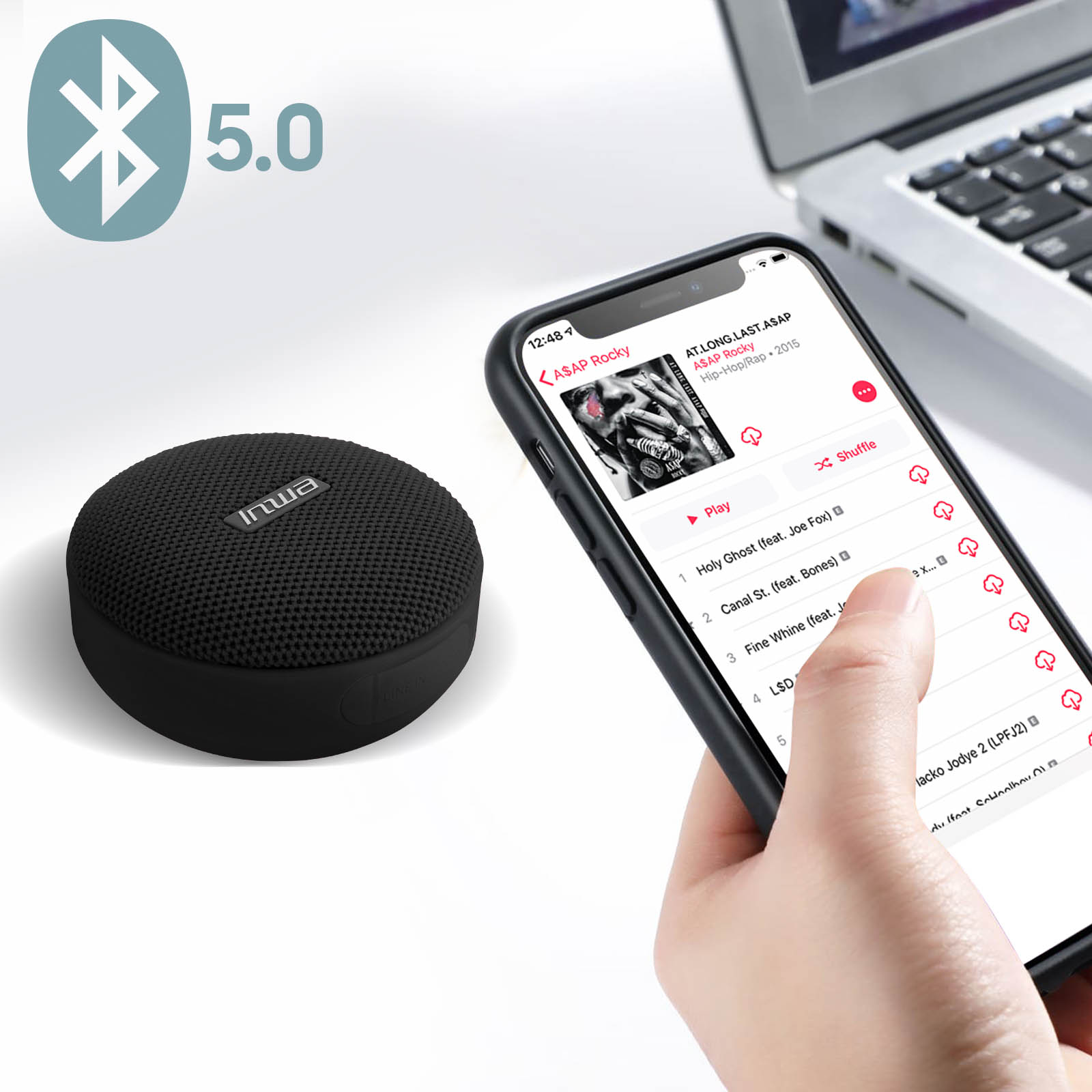 Un haut-parleur noir à côté d'un téléphone affichant une application musicale. Le haut-parleur est petit et rond, avec un symbole bluetooth.