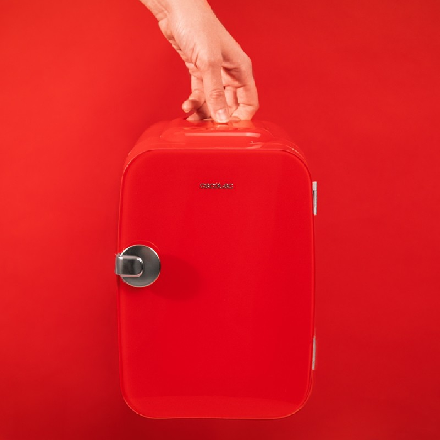 Una mini-nevera roja con un asa plateada y una mano sosteniendo su asa superior.