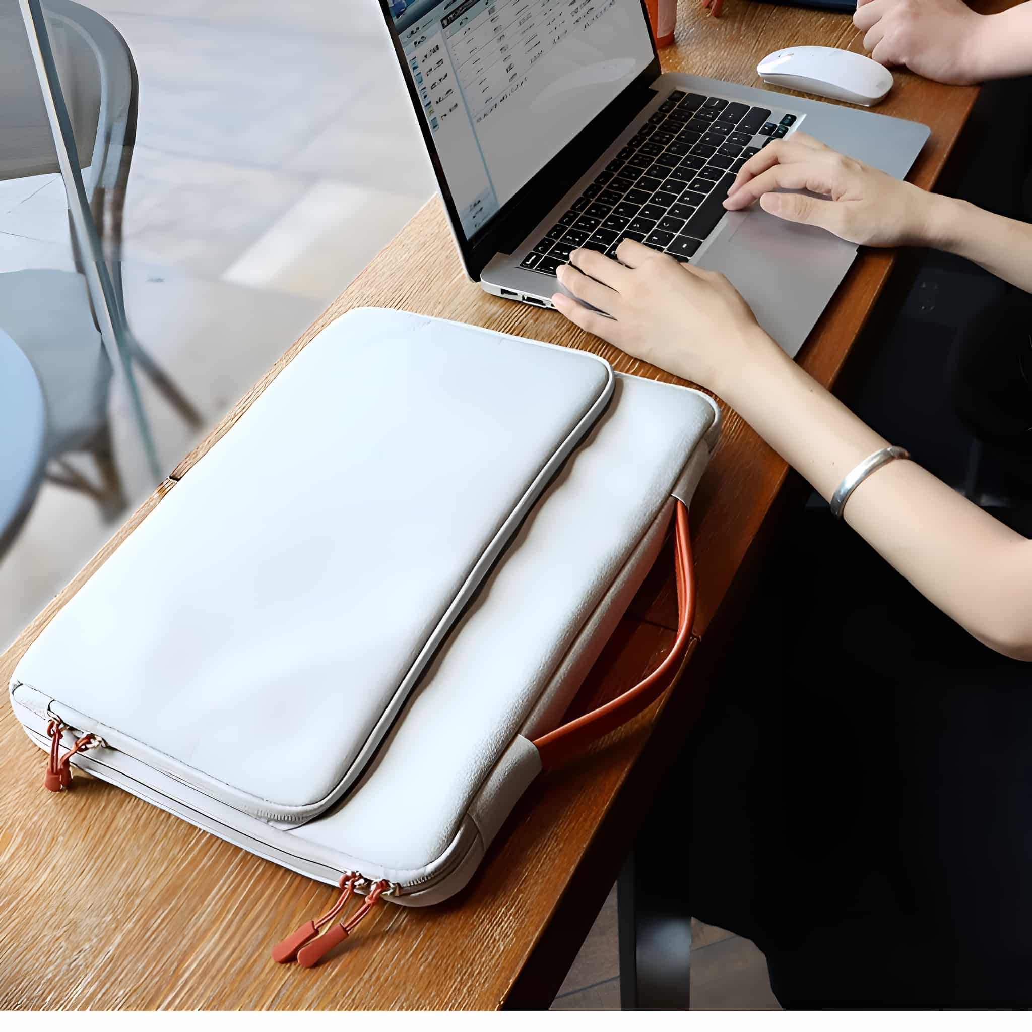 Eine Person an einem Holztisch benutzt einen Laptop mit einer weißen Laptoptasche.