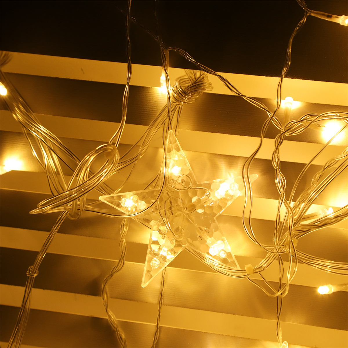 Nahaufnahme von sternförmigen Lichterketten, die einen weißen, lamellenartigen Hintergrund beleuchten.