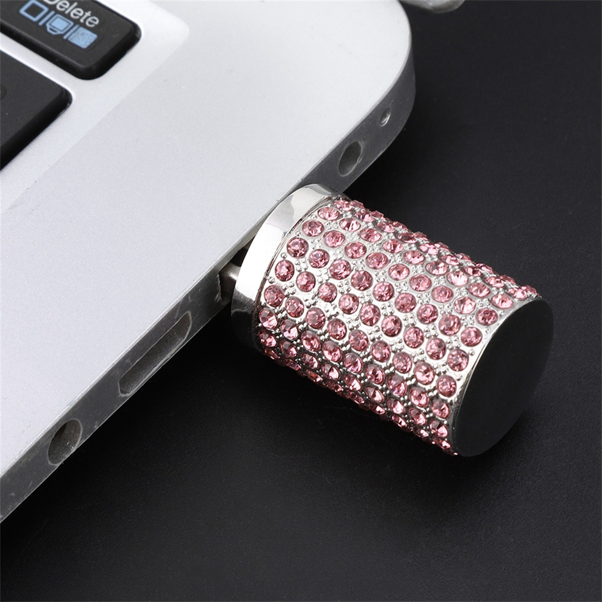 Ein USB-Stick mit rosa Strasssteinen, der an einen Laptop angeschlossen ist. Schwarzer Hintergrund.