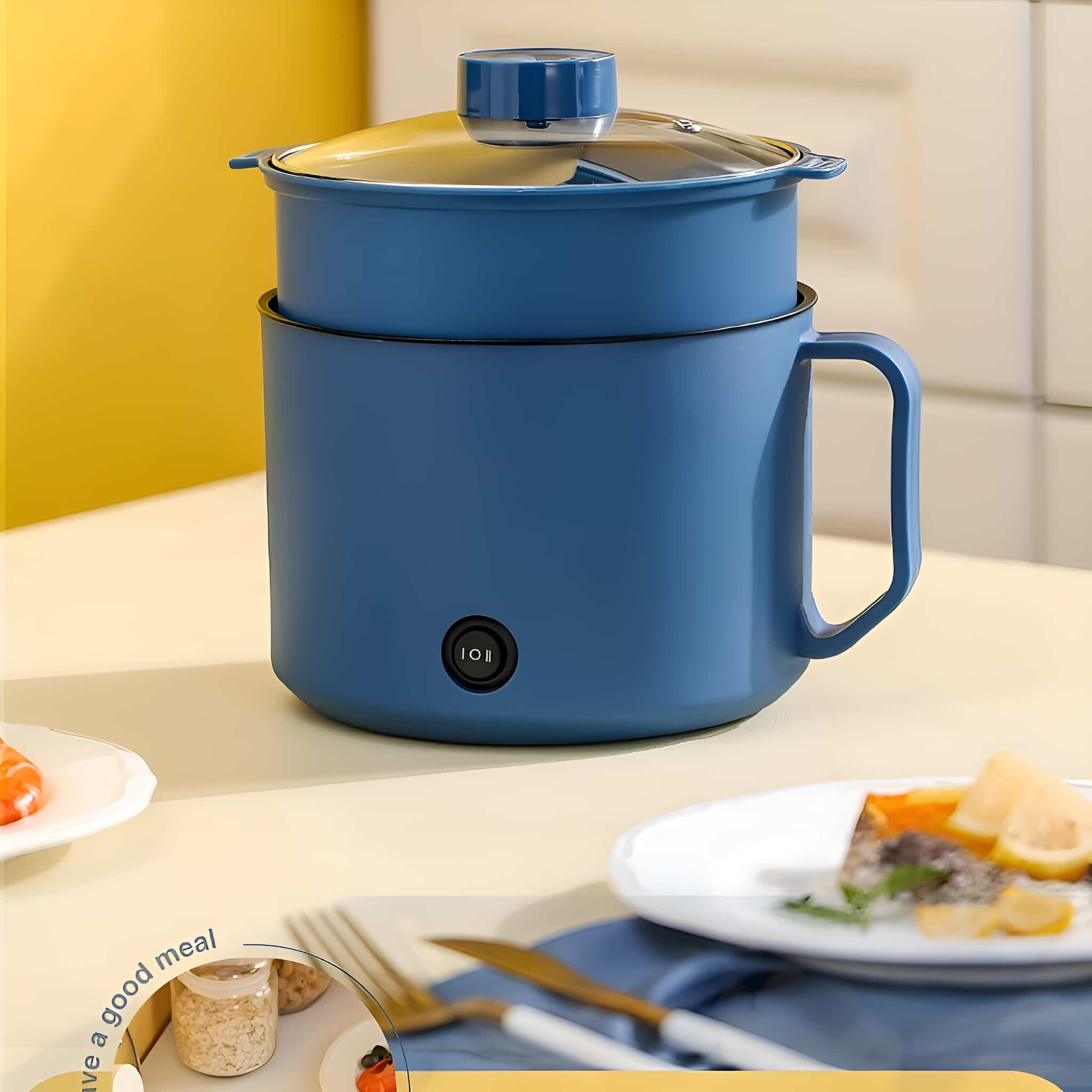 Ein blauer elektrischer Kochtopf mit Griff und Deckel. Er steht auf einem Tisch mit Lebensmitteln wie Zitrone und Fisch.