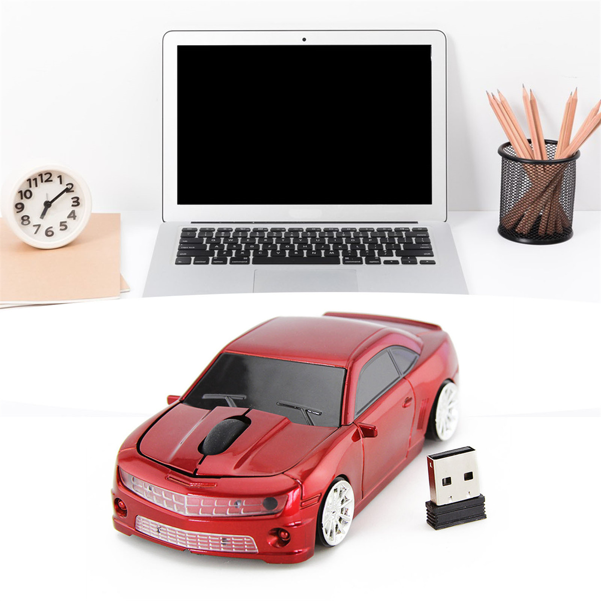 Eine rote, auto-förmige Computermaus mit USB-Empfänger und schwarzem Laptop auf weißer Oberfläche.