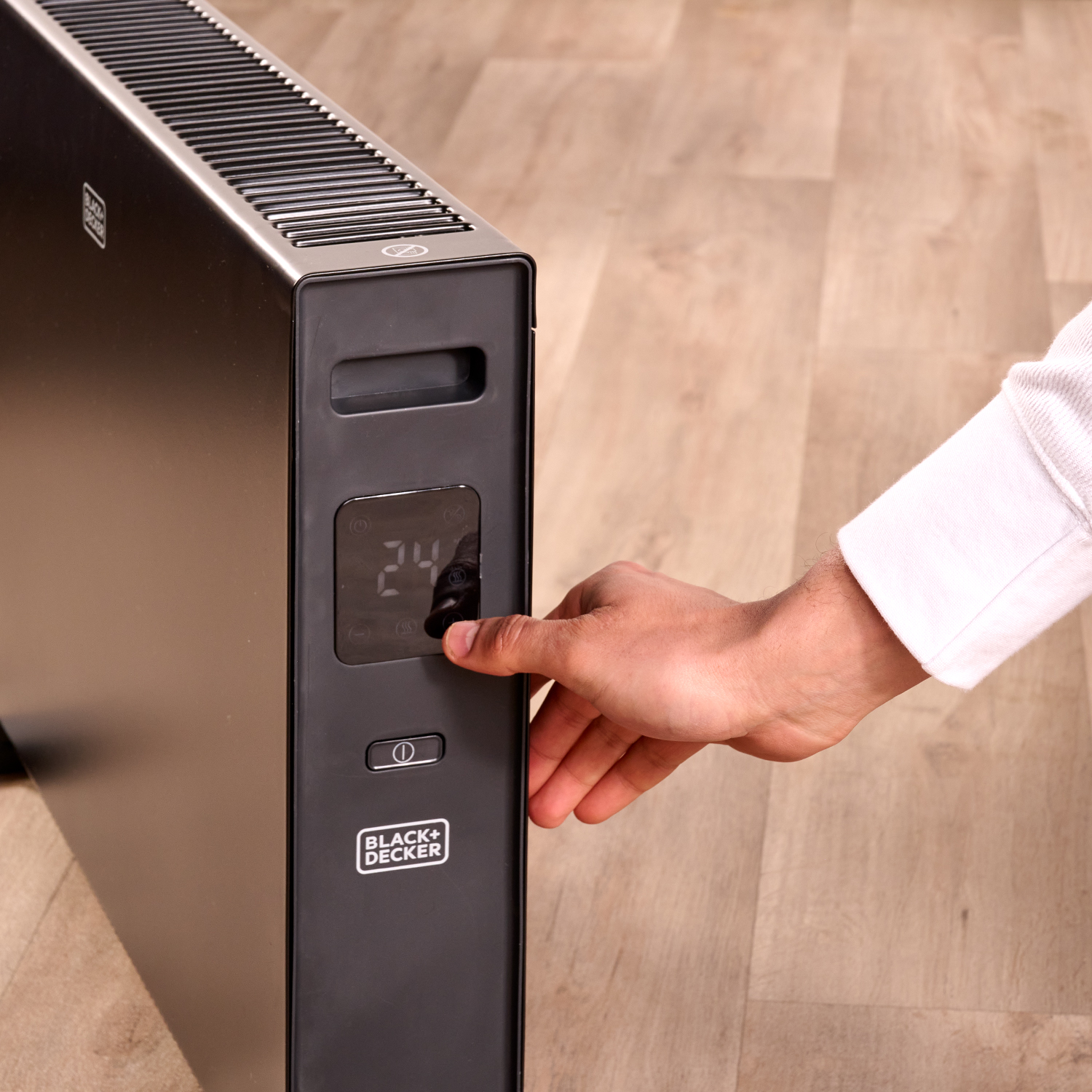 Ręka osoby kręci pokrętłem na czarno-srebrnym grzejniku Black+Decker.