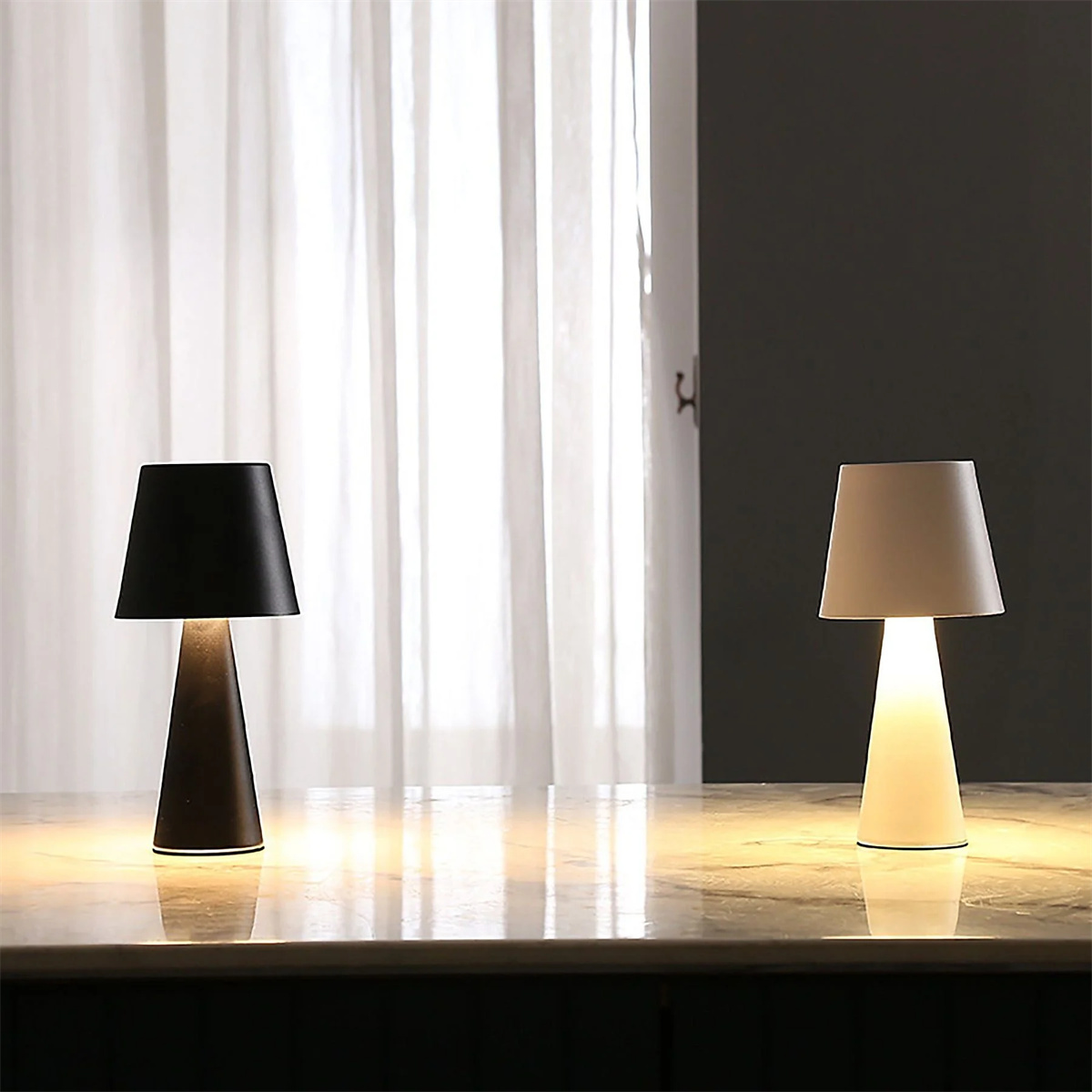 Zwei Tischlampen. Eine ist schwarz, die andere weiß. Beide haben einen konischen Sockel.
