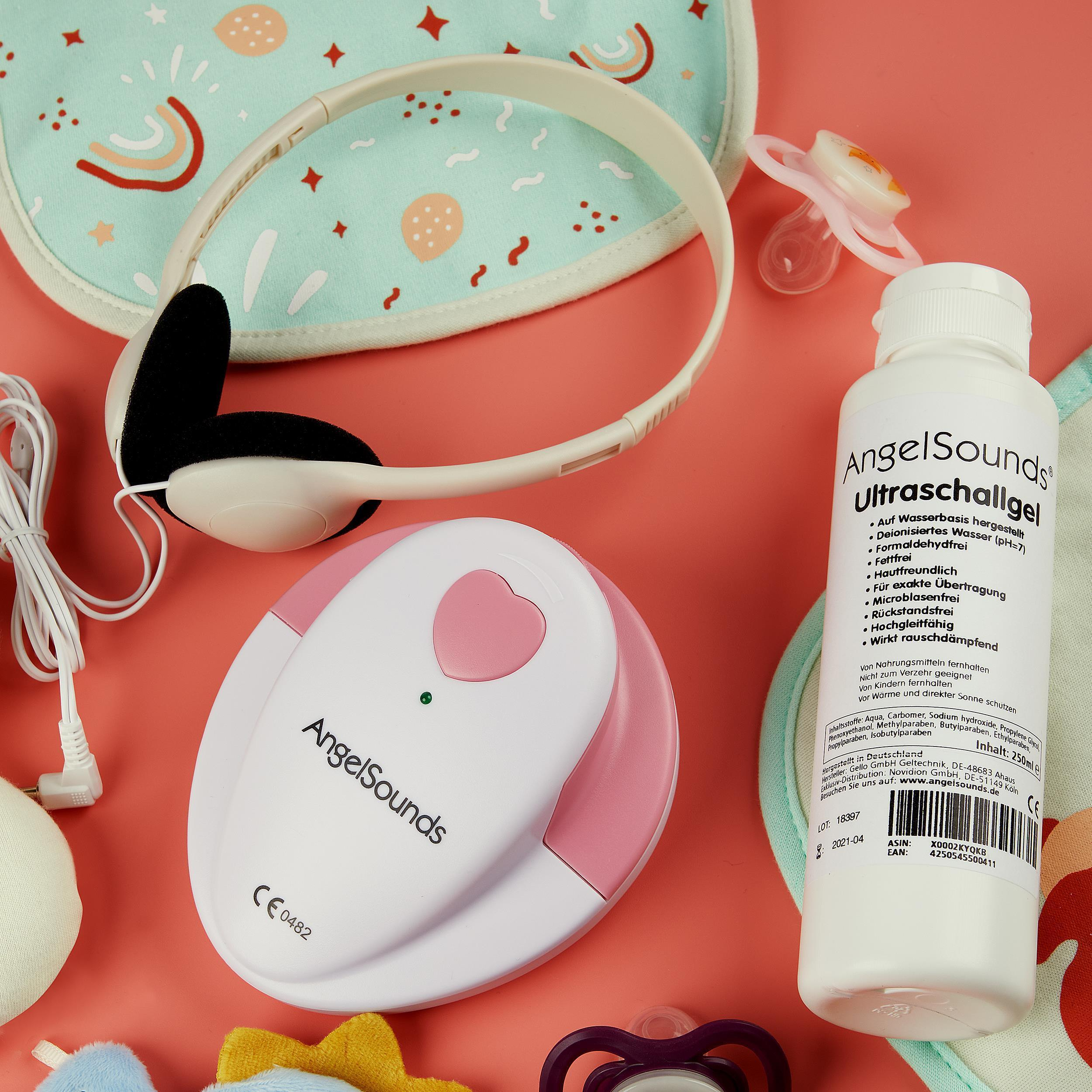 Babyartikel: Kopfhörer, Gel, Lätzchen, Schnuller und ein Babyphone. Pinker Hintergrund. Artikel sind auf einem Tisch angeordnet.