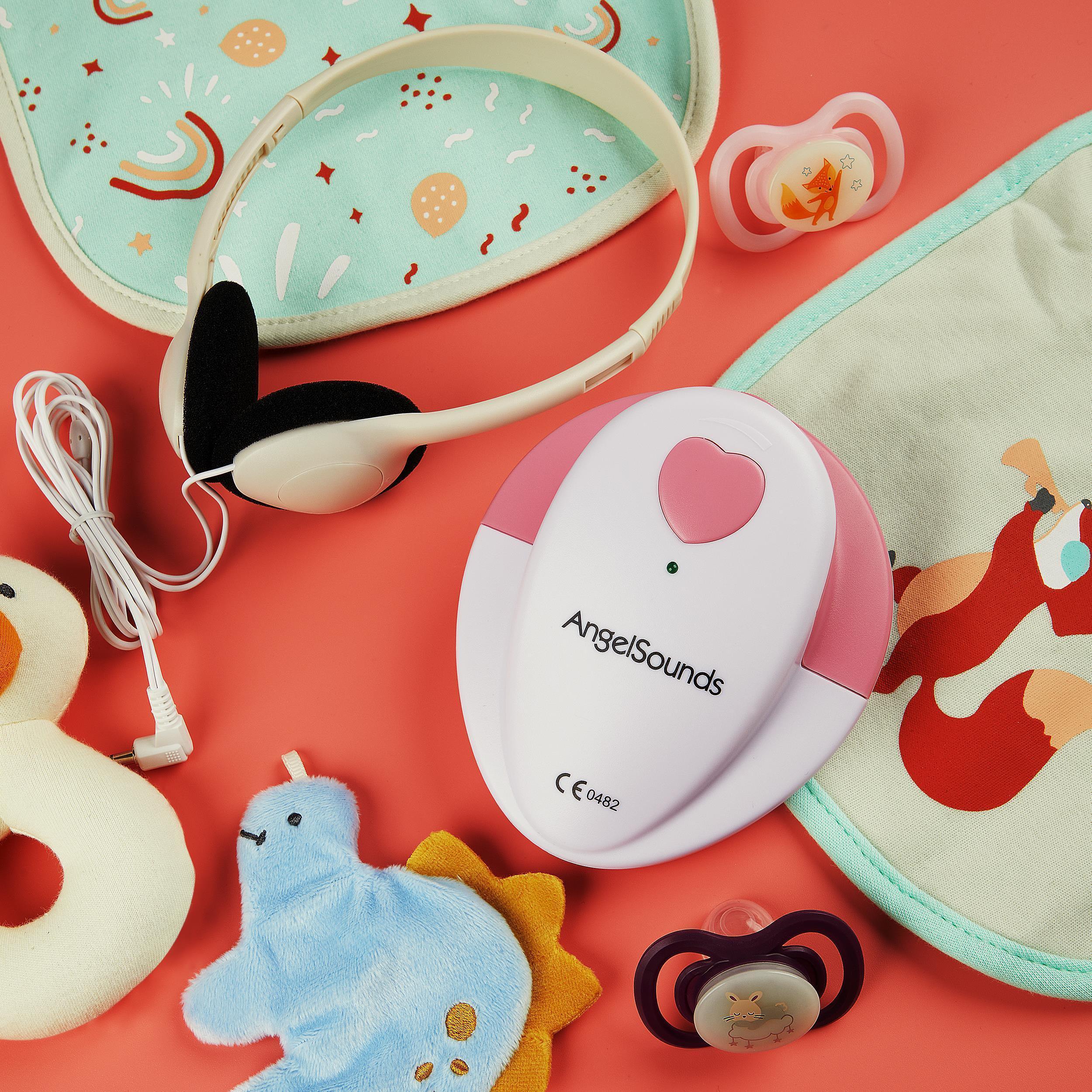 Babyphone-Set mit Lätzchen, Schnullern, Kopfhörern und einem Baby-Soundgerät auf roter Oberfläche.