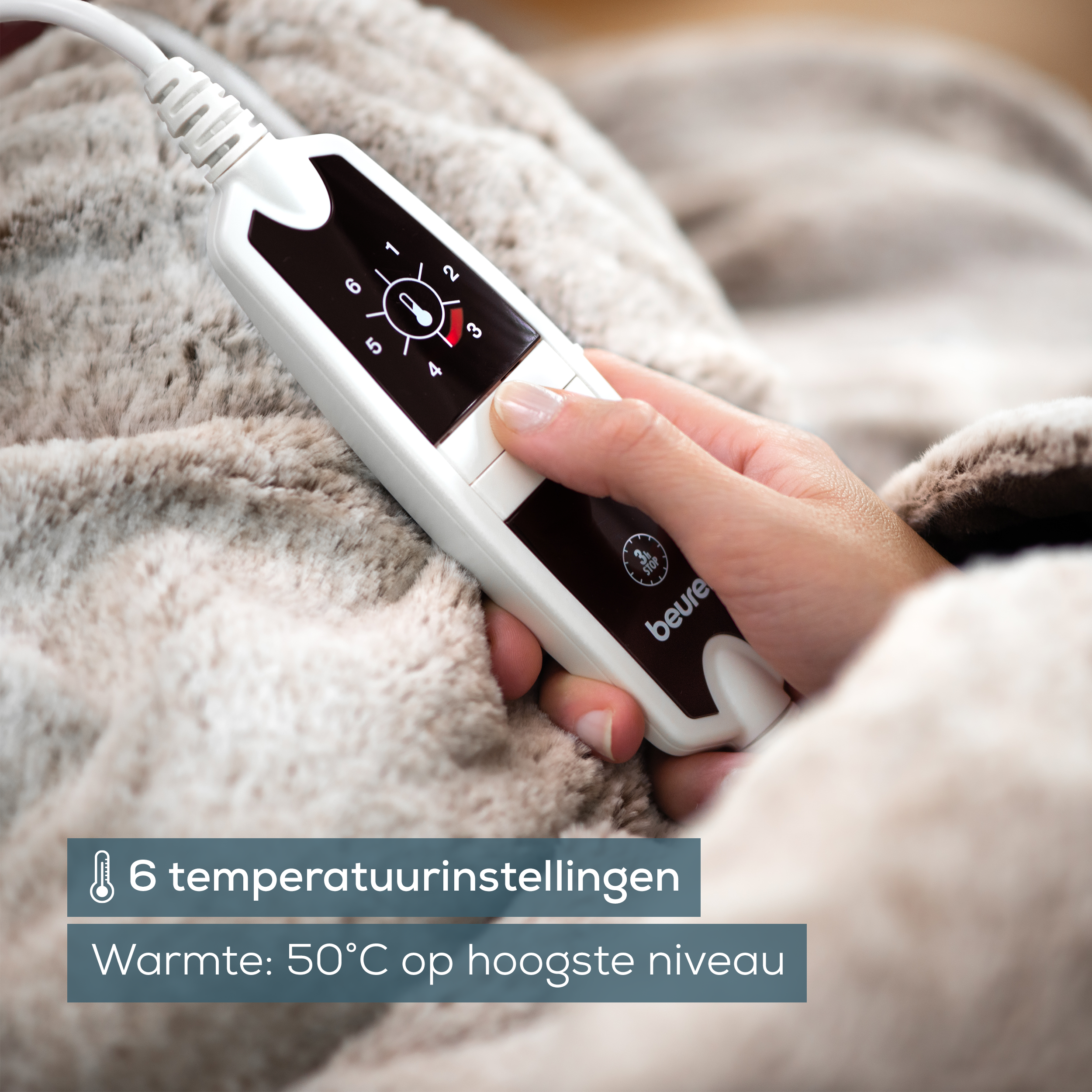 Eine Hand berührt ein weißes Bedienfeld mit Temperatureinstellungen auf einer flauschigen Decke.