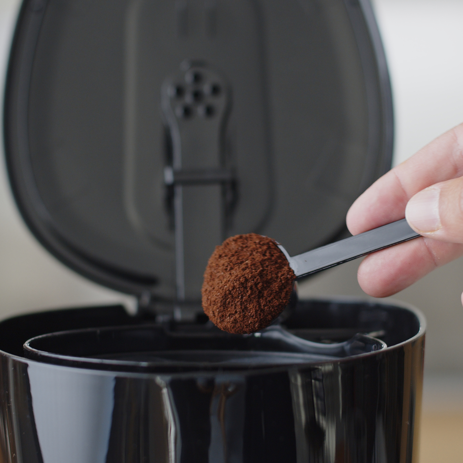 Osoba dodaje zmieloną kawę do ekspresu do kawy za pomocą czarnej miarki.