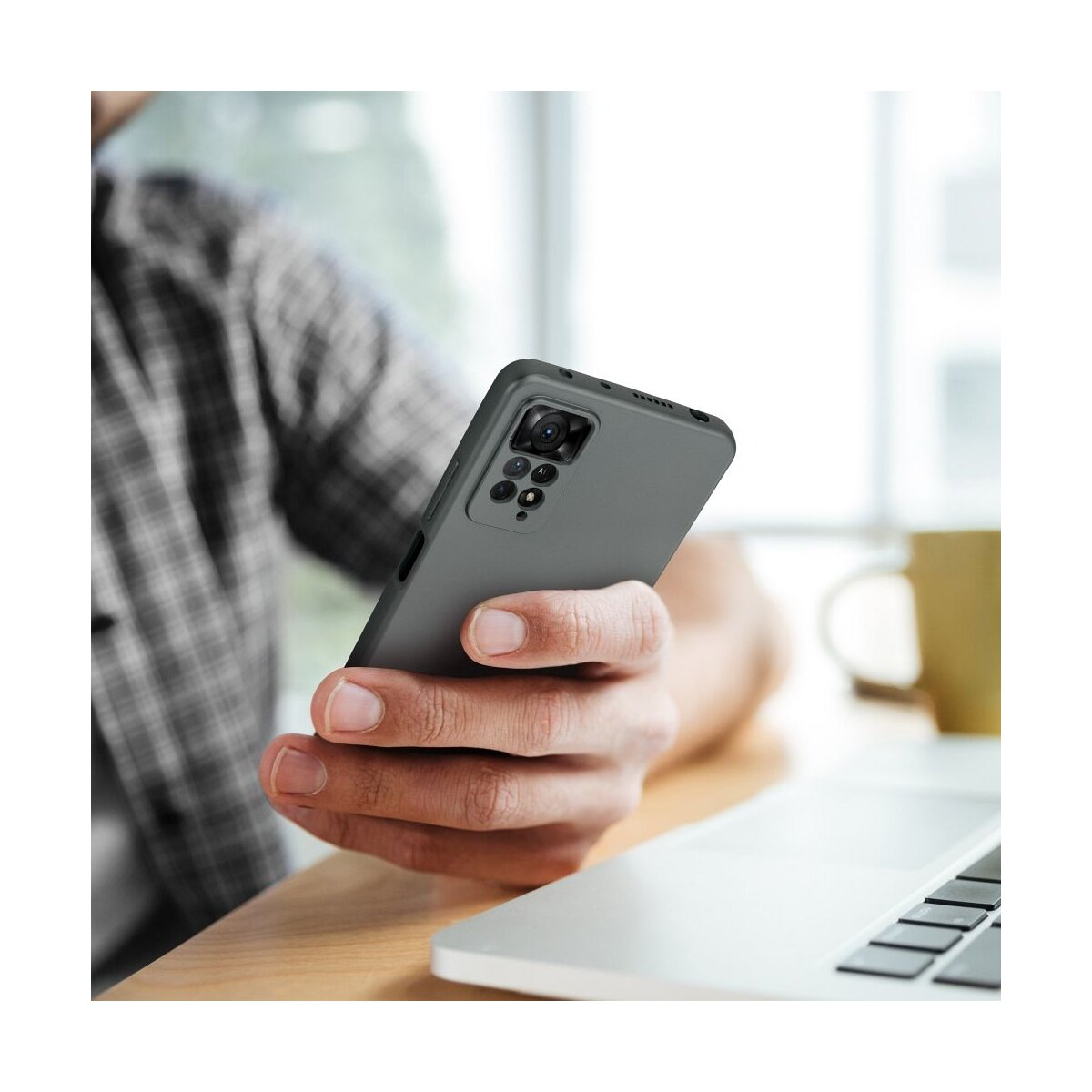 Persona che tiene un telefono grigio con custodia, vicino a un laptop.