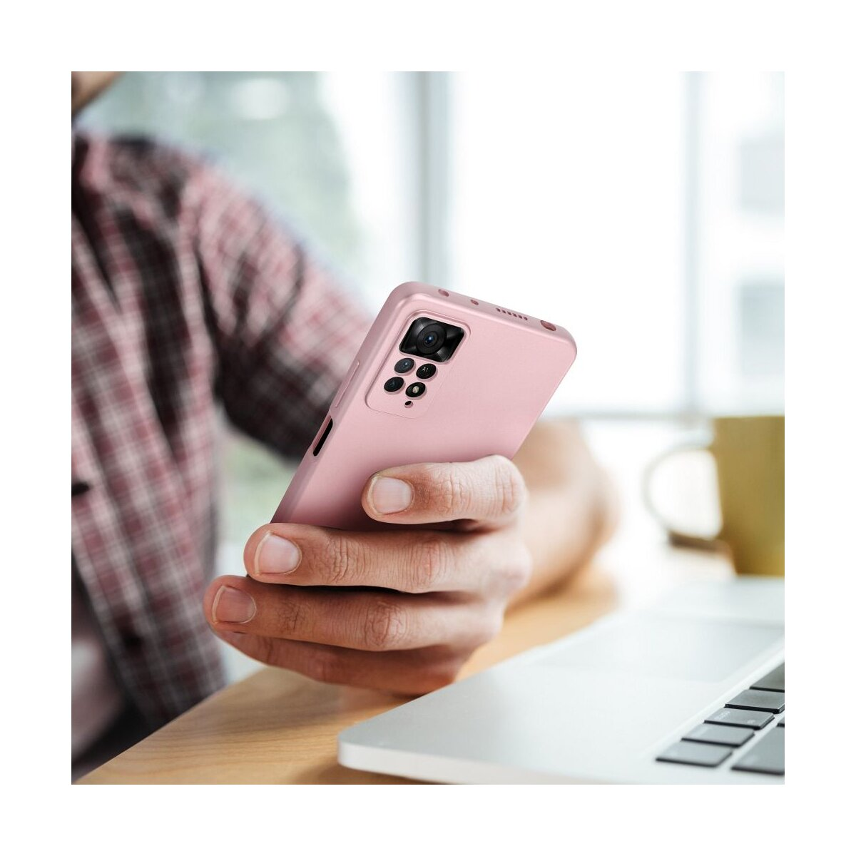 Persona che tiene un telefono rosa in una custodia rosa. Lo sfondo include un laptop e una tazza. Sfondo sfocato.