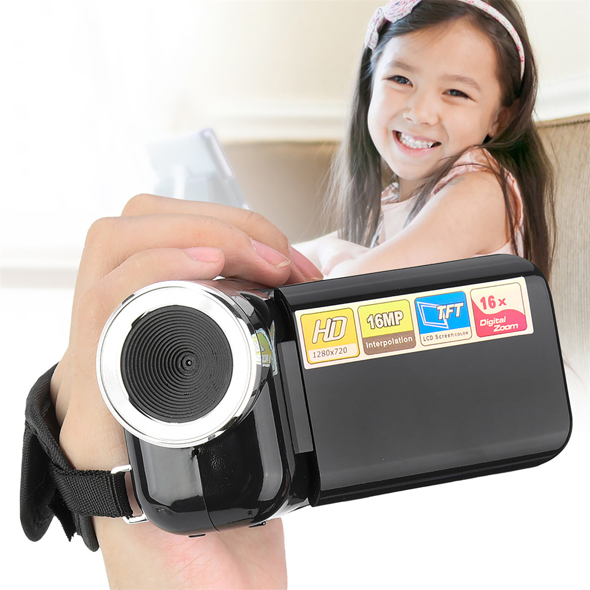Eine Person hält eine schwarze Kamera mit Bildschirm, HD, 16MP und 16x Zoom-Etiketten. Ein Mädchen lächelt im Hintergrund.