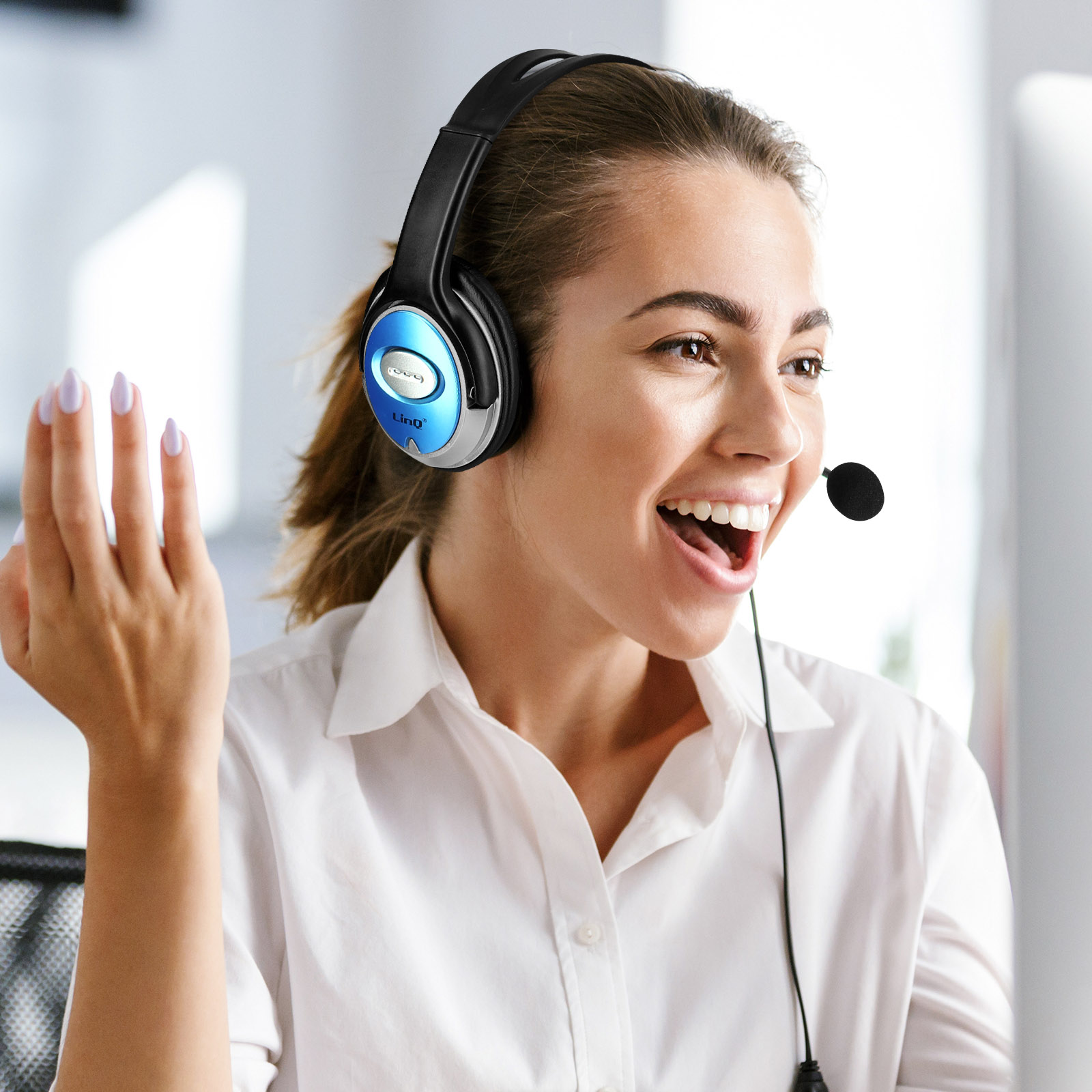 Une femme avec un casque souriant. Elle porte une chemise blanche et regarde un ordinateur.