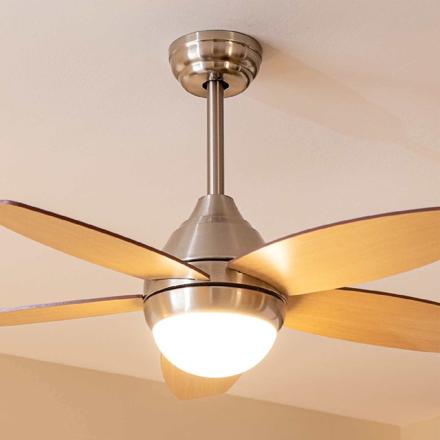 Un ventilatore da soffitto con cinque pale in legno e un'illuminazione. Montato su un soffitto bianco.