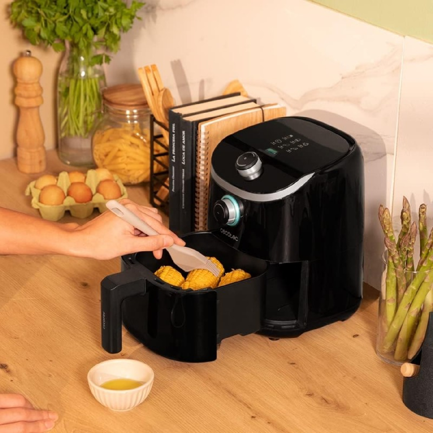 Eine Heißluftfritteuse mit Essen darin, eine Person nimmt mit einer Zange Essen heraus.
