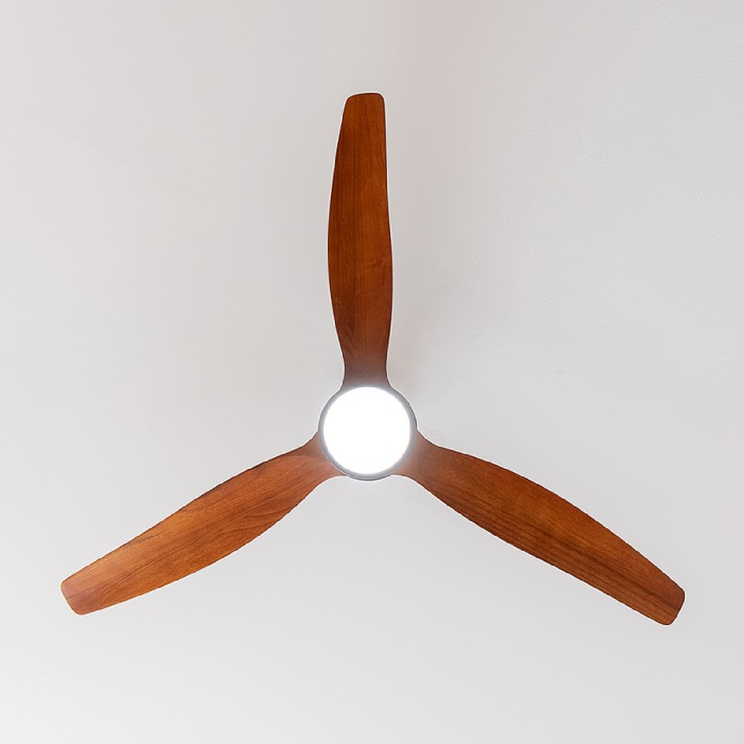 Un ventilador de techo con tres aspas de madera y una lámpara central, visto desde abajo.