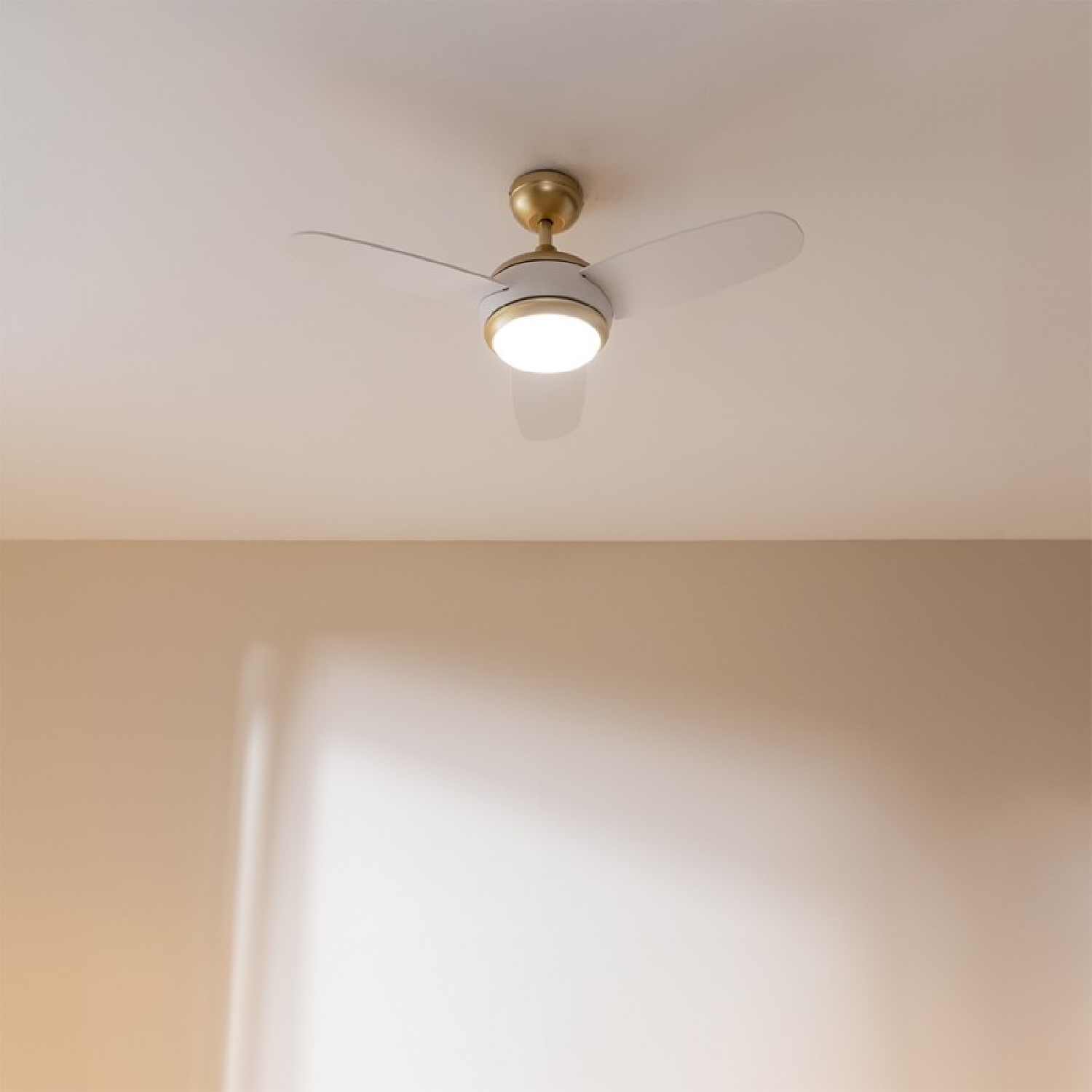 Ventilatore da soffitto bianco con tre pale e luce centrale, appeso a un soffitto bianco.