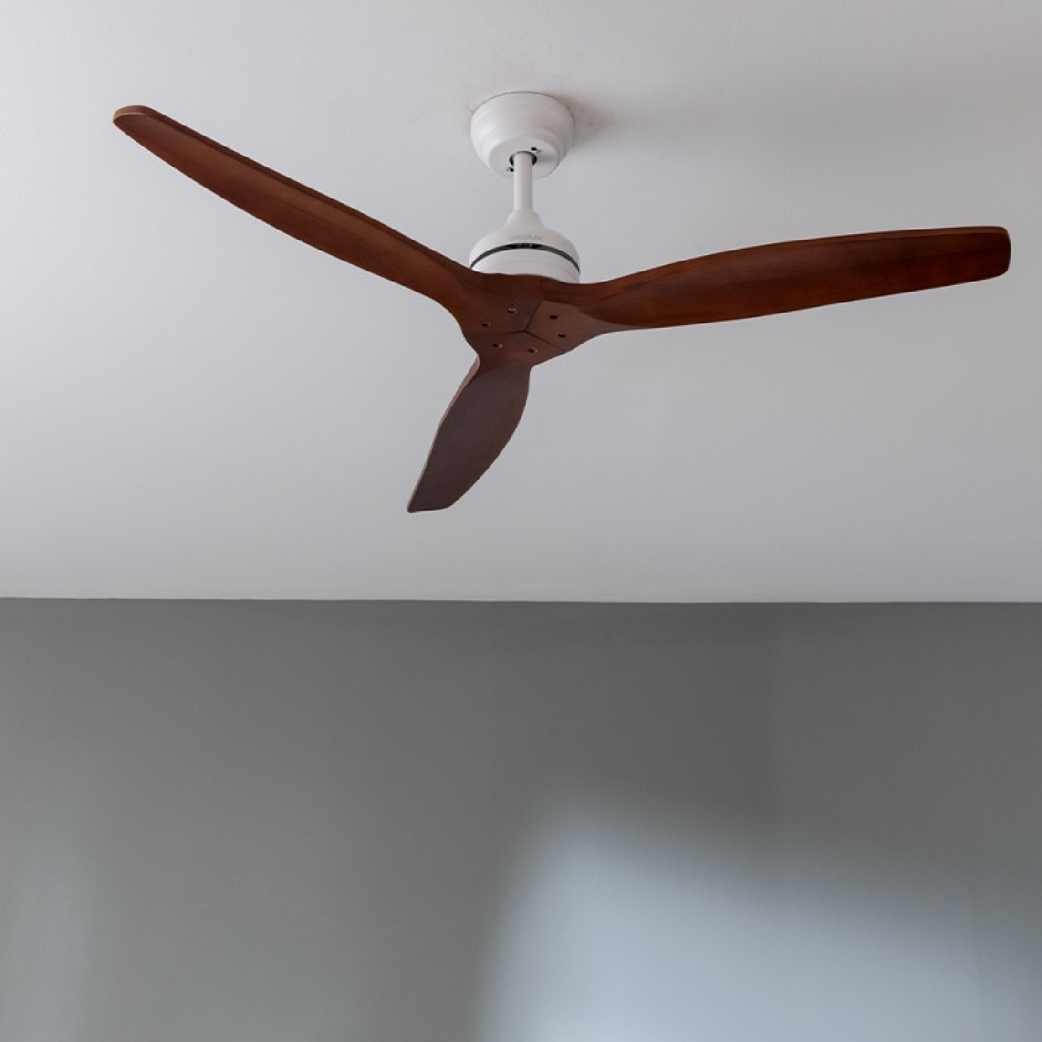 Ventilatore da soffitto con tre pale in legno contro un soffitto bianco e un muro grigio.