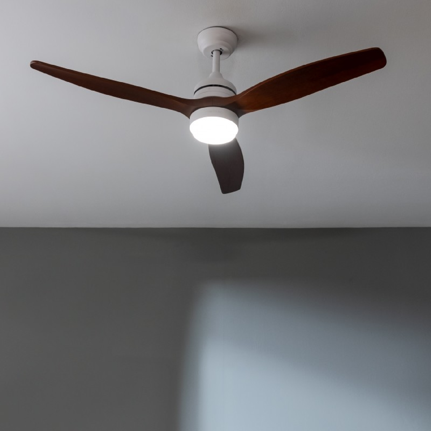 Deckenventilator mit drei dunkelbraunen Holzflügeln und weißem Motorgehäuse.
