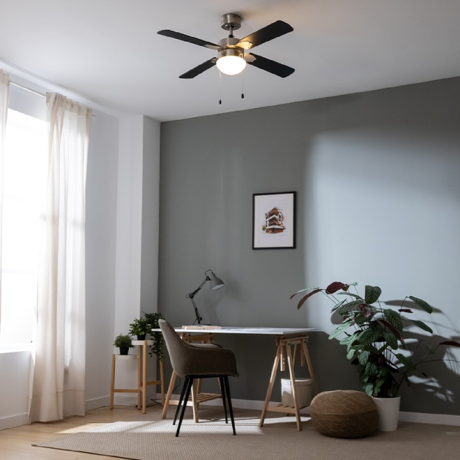 Stanza con ventilatore a soffitto, scrivania, sedia e piante. Parete grigia, finestra con tende e immagine.