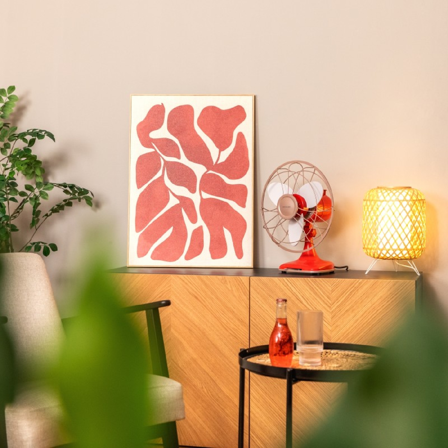 Ventilatore rosso e un quadro su un mobile in legno, con lampada e bevanda.
