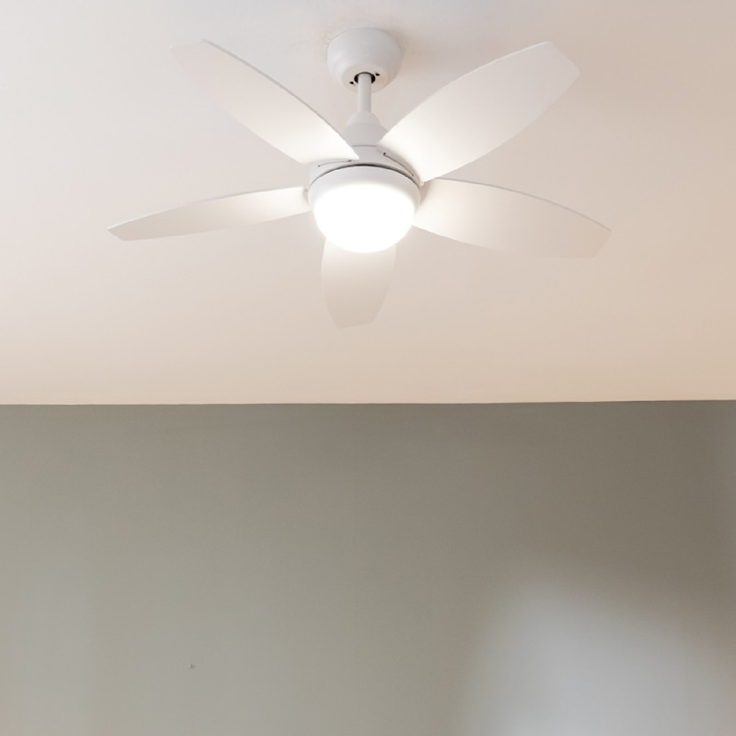 Ventilatore a soffitto bianco con cinque pale e luce centrale, su sfondo grigio.