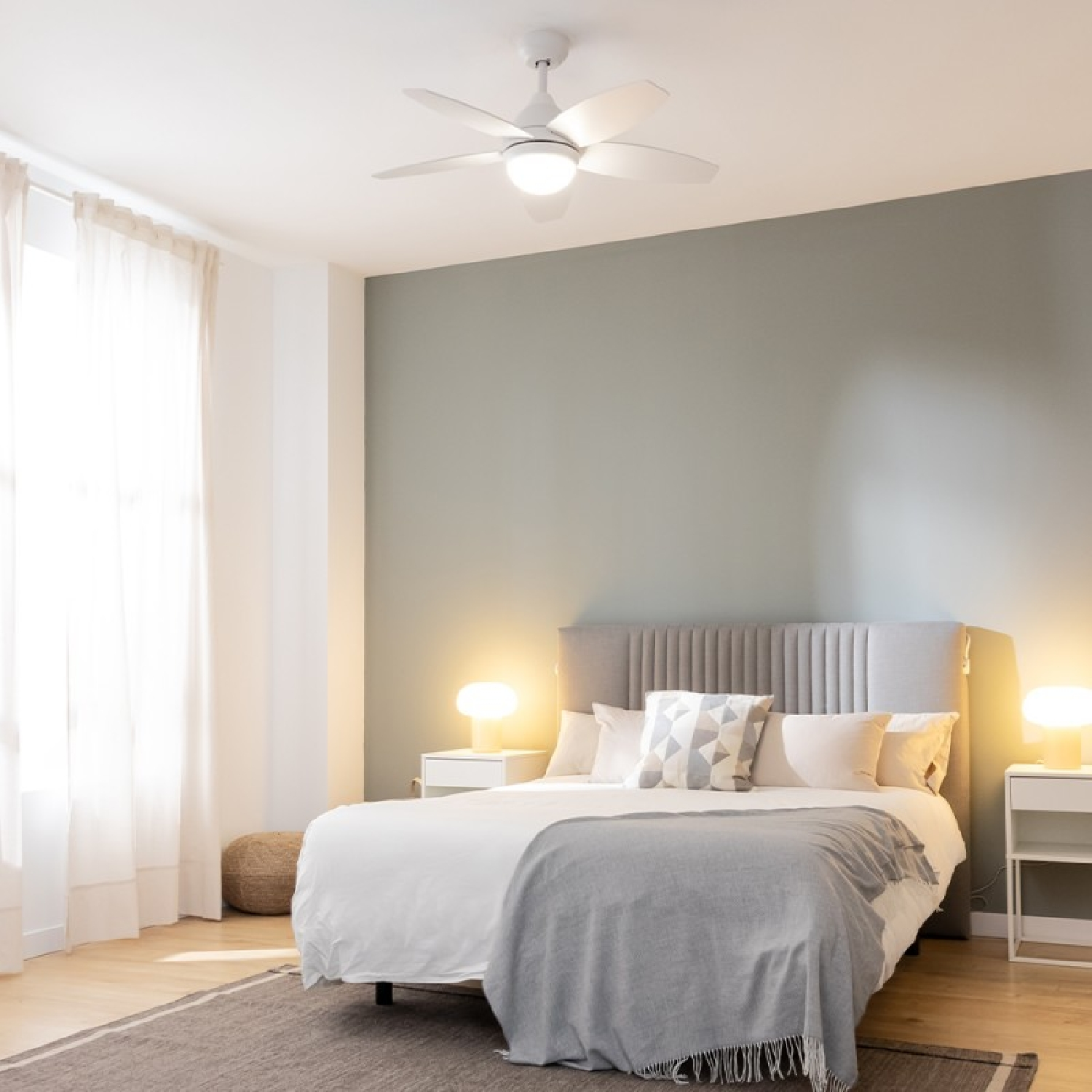 Una camera da letto con un ventilatore a soffitto, un letto con una coperta grigia e una parete verde.