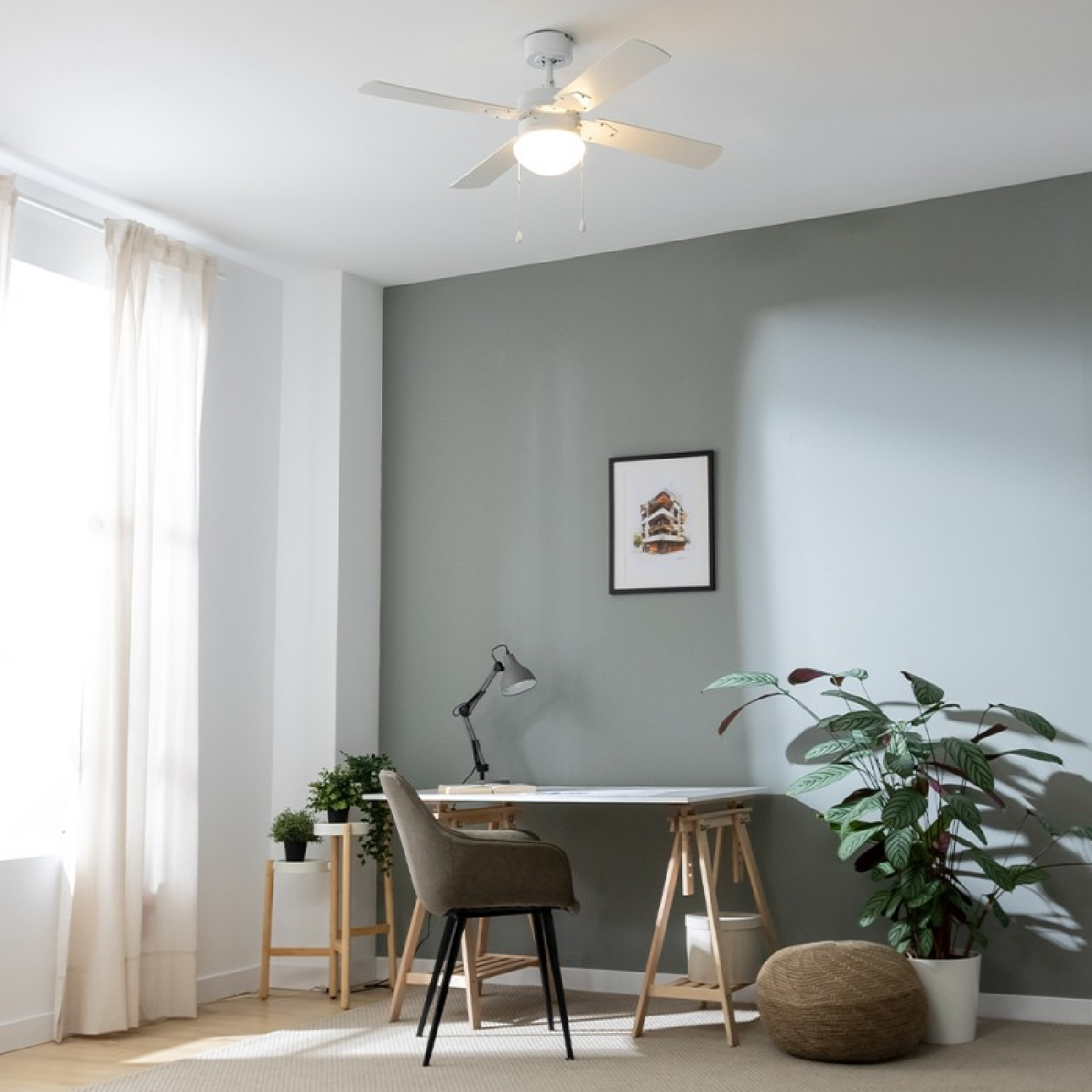 Una stanza con ventilatore a soffitto, scrivania, sedia e opere d'arte. Le pareti sono dipinte.