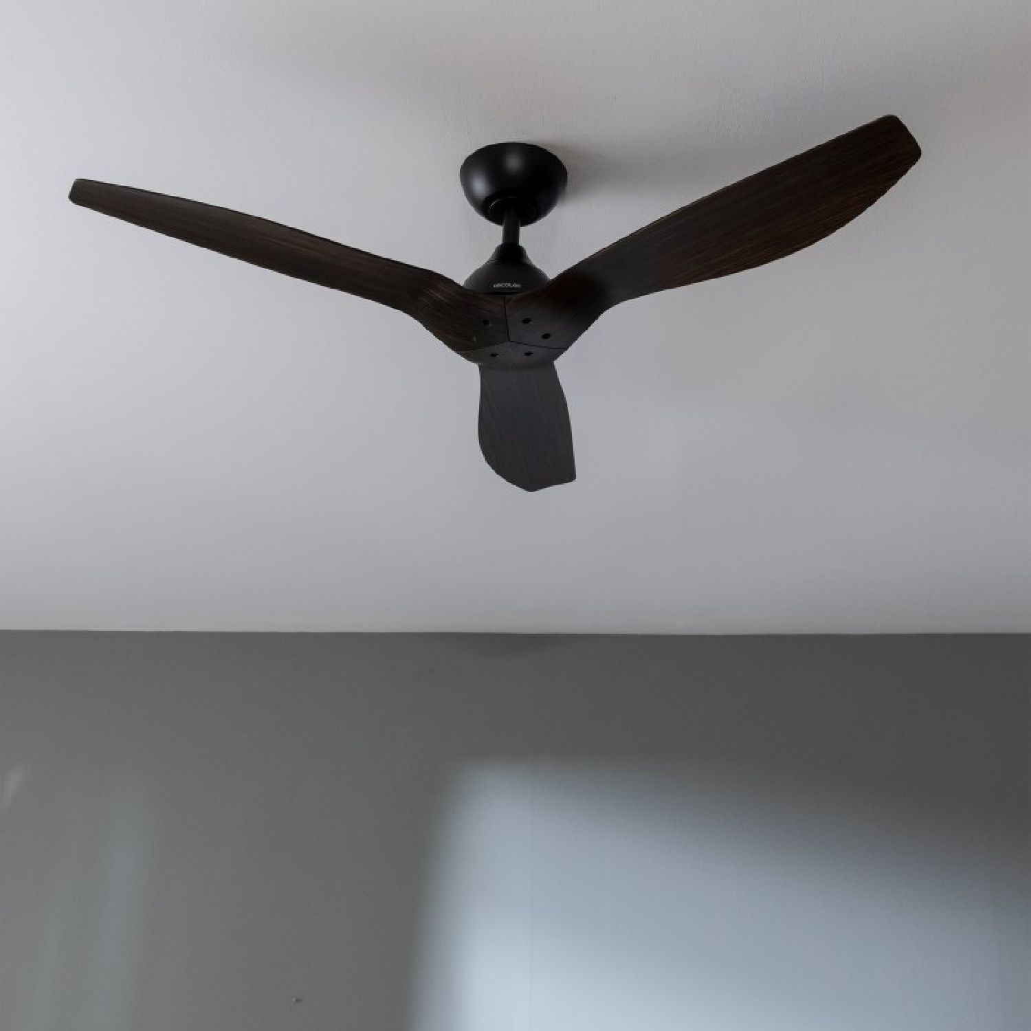 Ein dunkler Deckenventilator aus Holz mit drei Flügeln, an einer weißen Decke montiert.