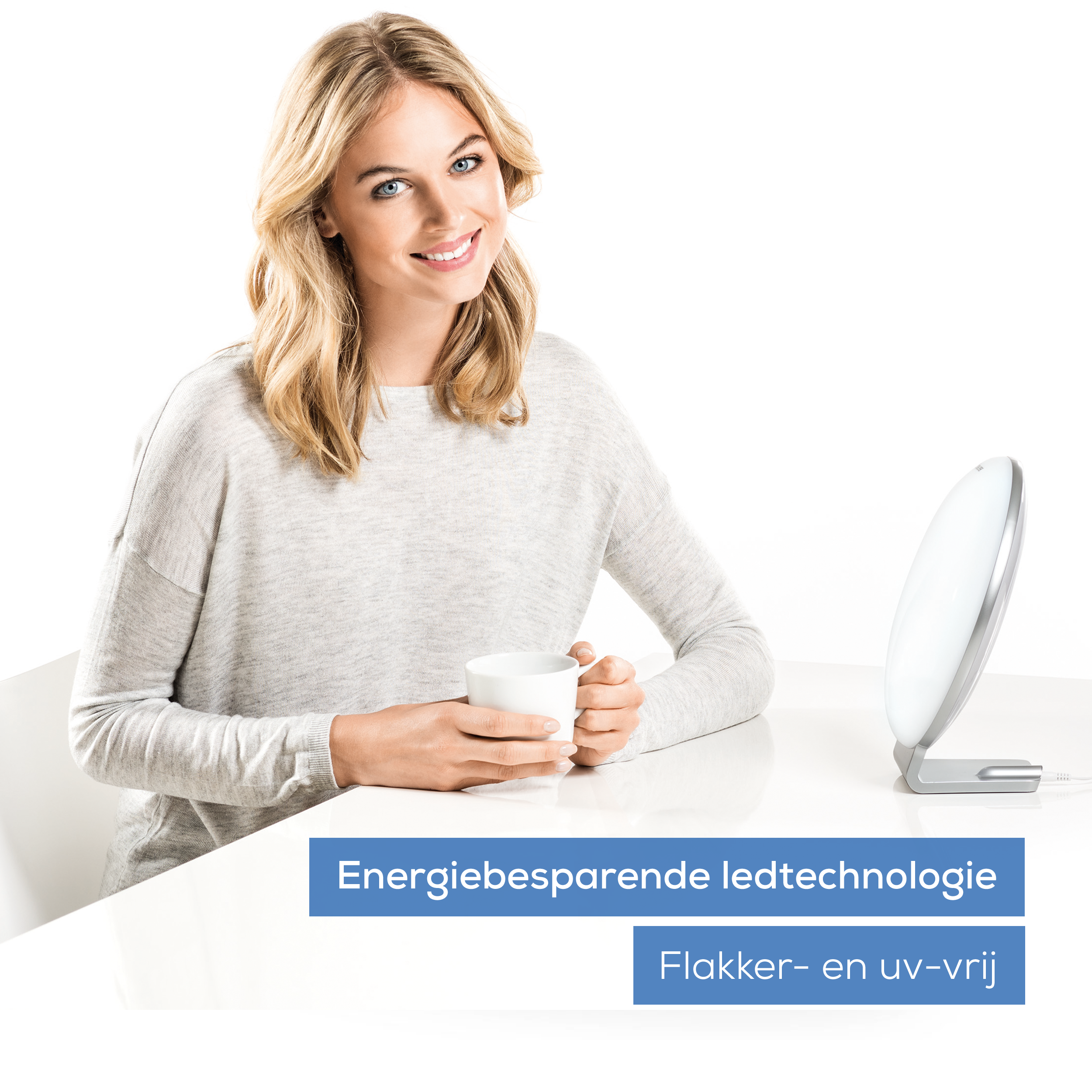 Blonde Frau lächelt, hält eine Tasse, in der Nähe einer weißen Lichttherapielampe. Weißer Hintergrund.