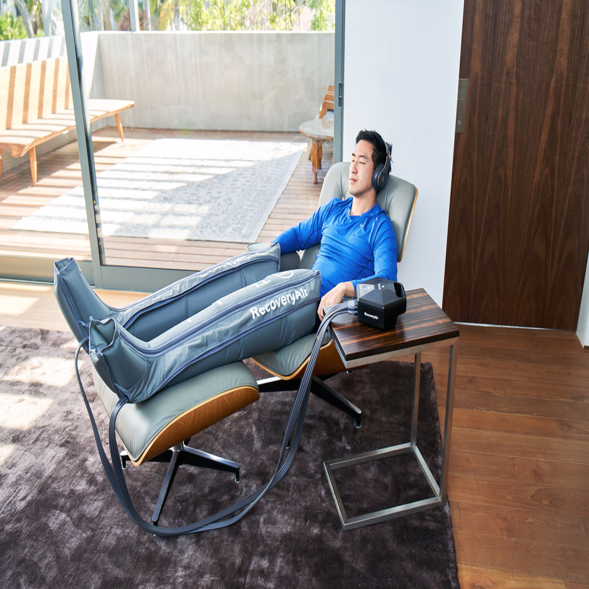 Un hombre con auriculares y mangas de compresión para las piernas se relaja en una silla. Hay una mesa cerca.
