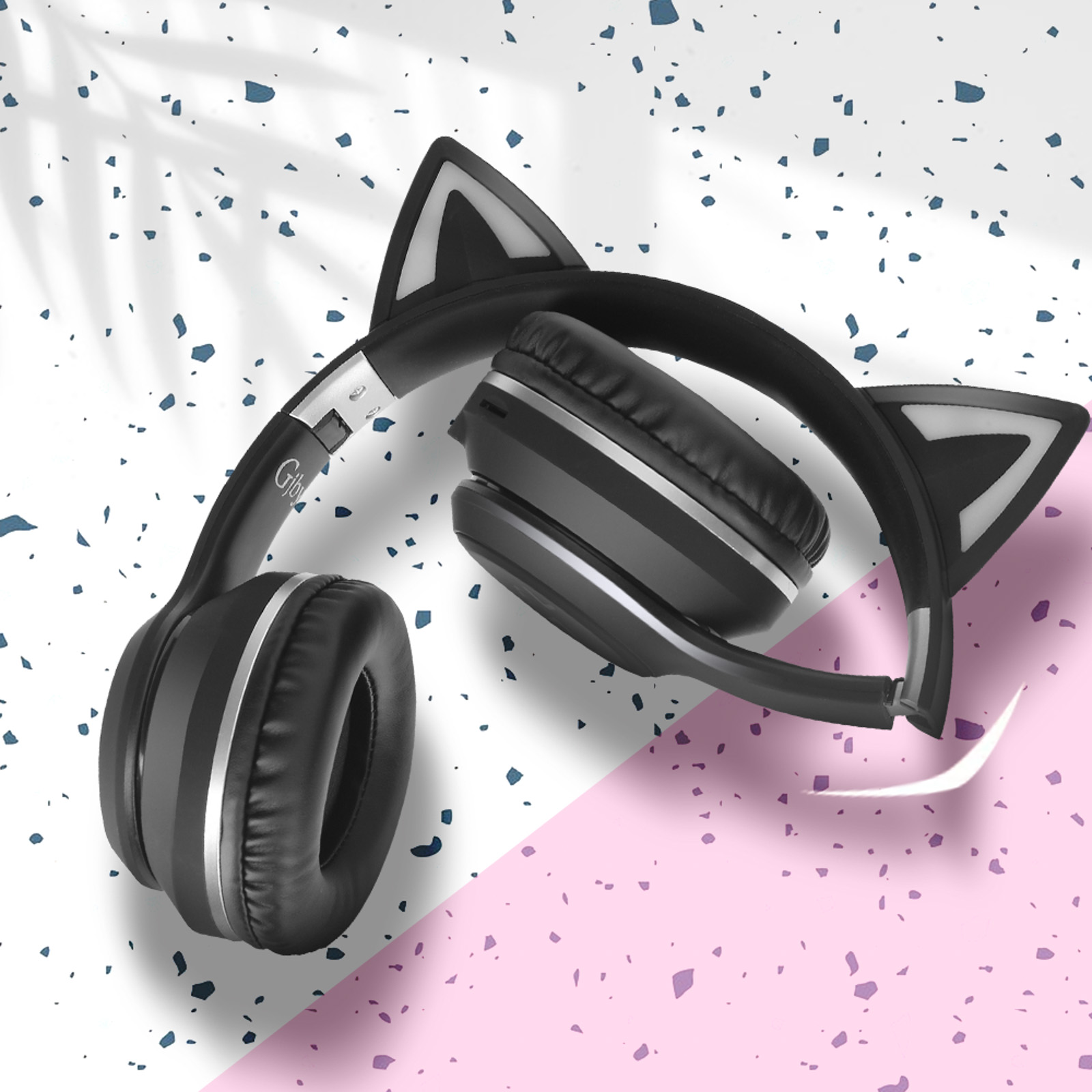 Casque noir avec oreilles de chat, plié sur une surface rose et blanche. Sans fil.