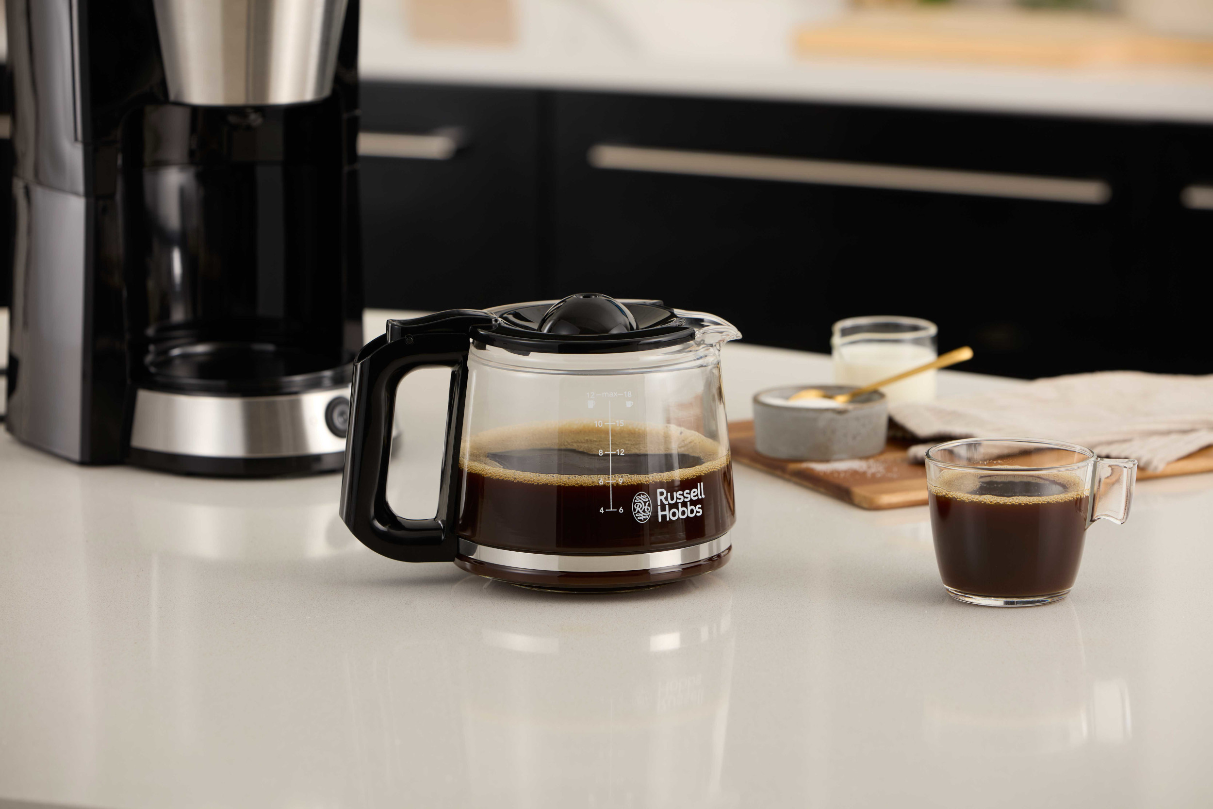 Ekspres do kawy ze szklaną karafką wypełnioną kawą. Na stole filiżanka i przekąski.